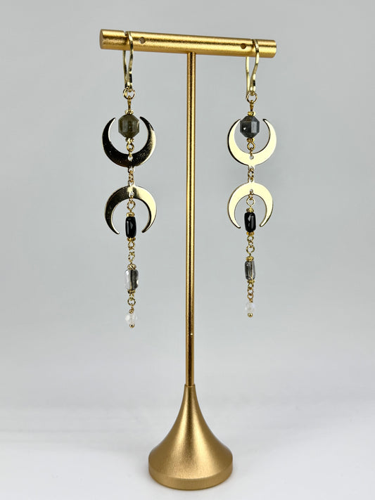 Pair of earrings with gold crescent moon designs on a gold stand against a gray background