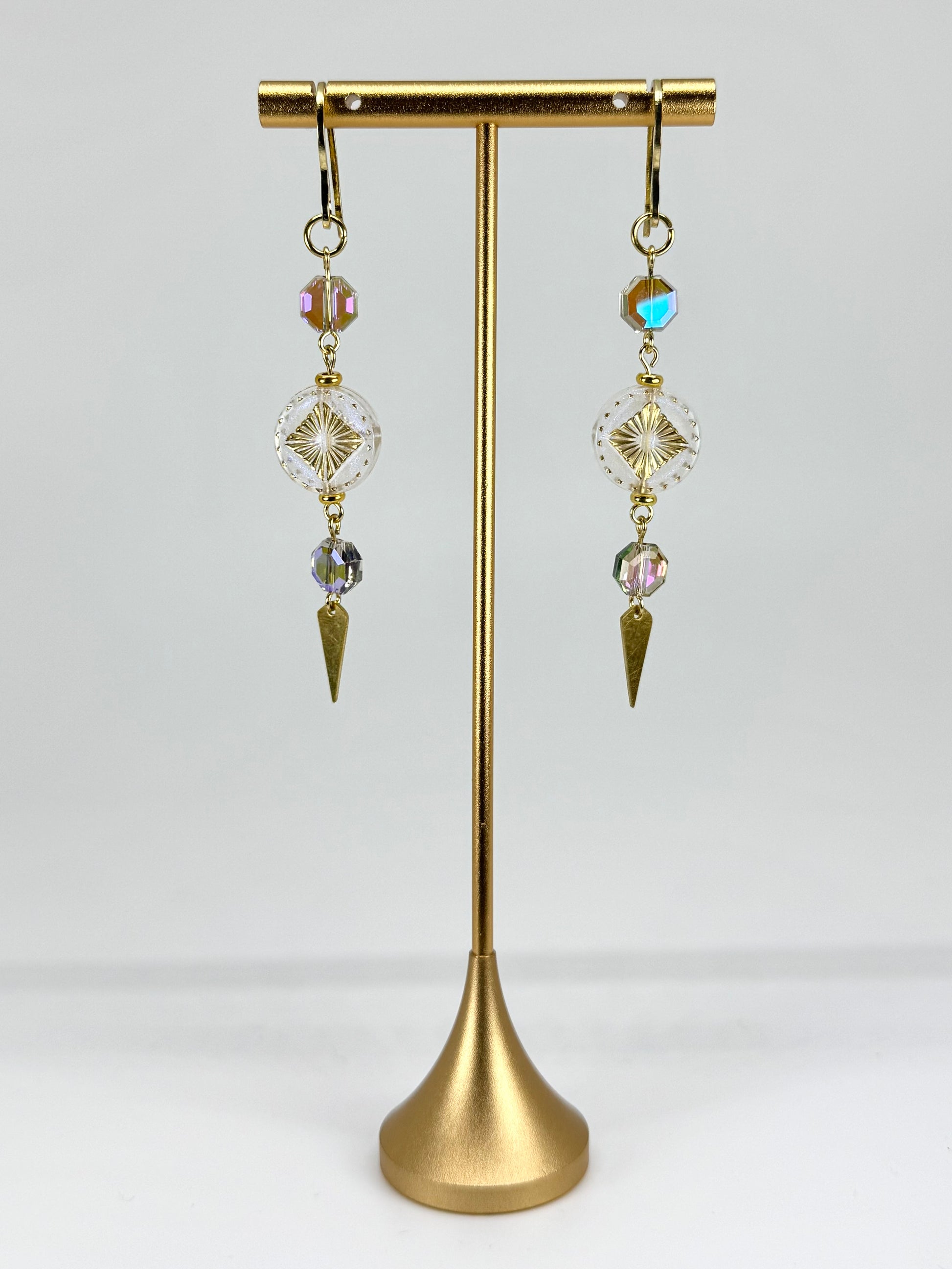 Pair of gold earrings with crystal beads on a gold stand against a white background
