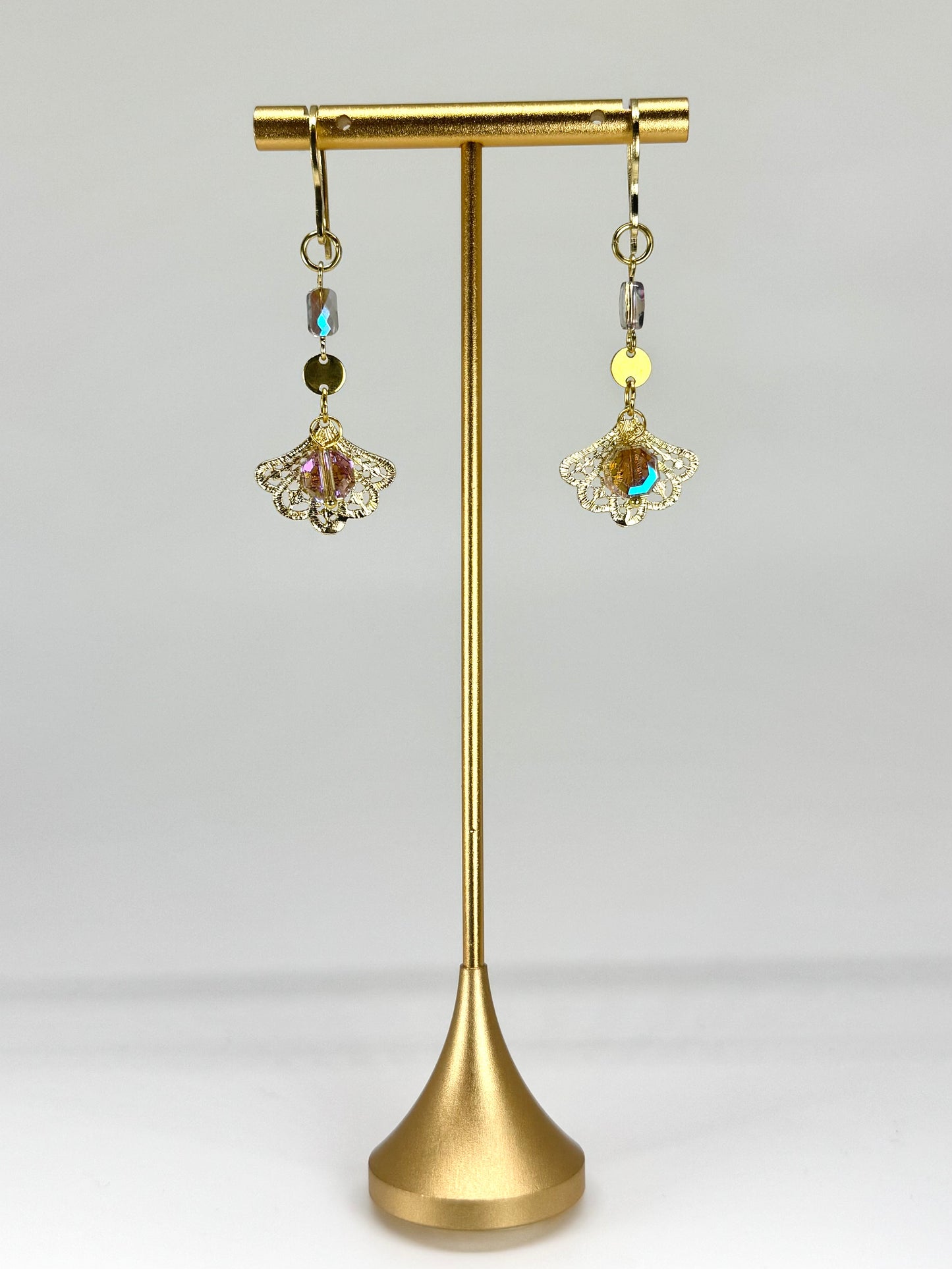 Gold earrings with gemstones on a gold stand against a white background