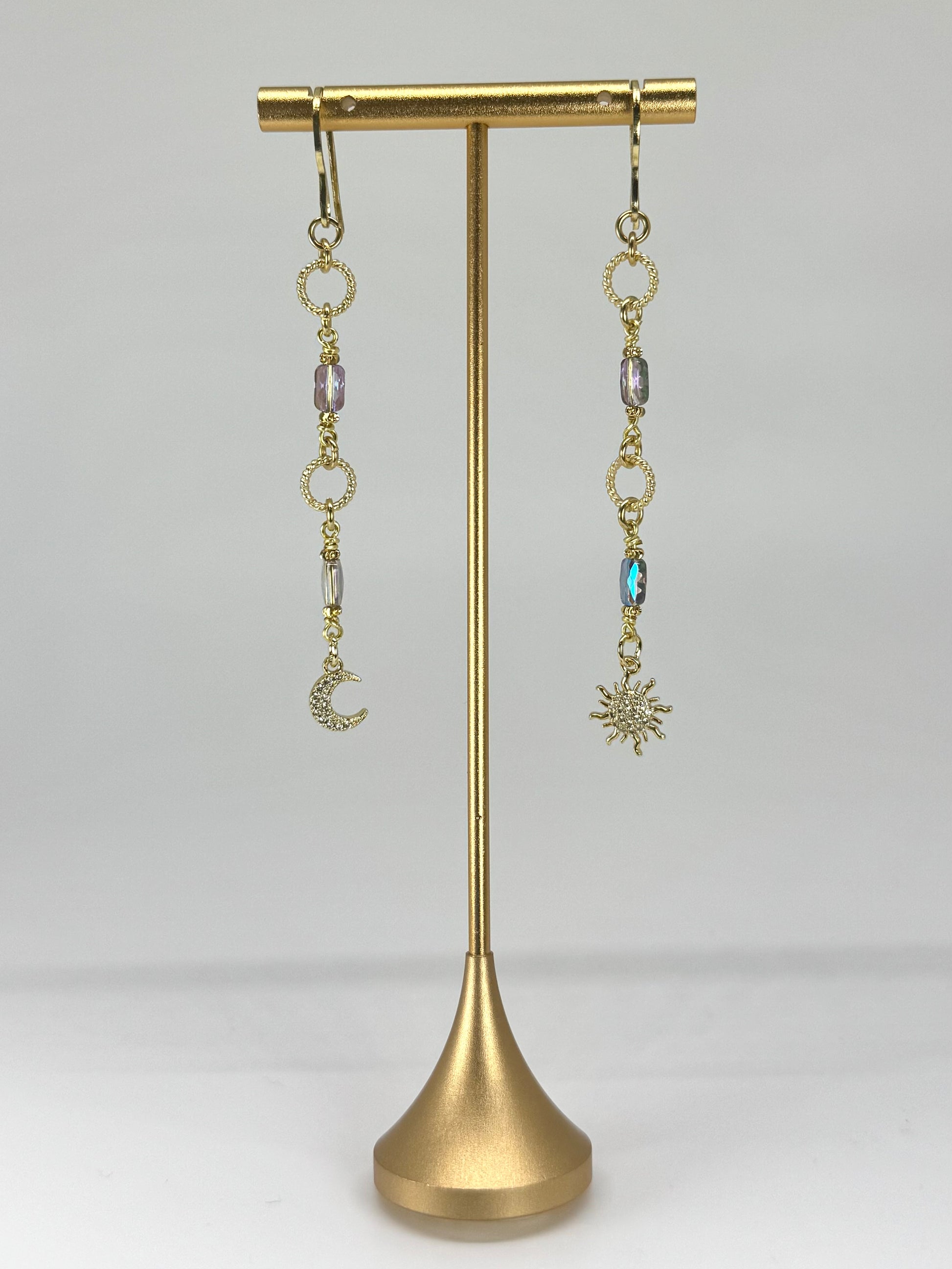 Gold earrings with charms on a gold stand against a white background