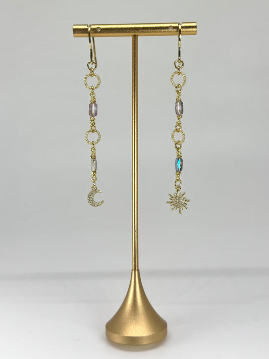 Gold earrings with charms on a gold stand against a white background