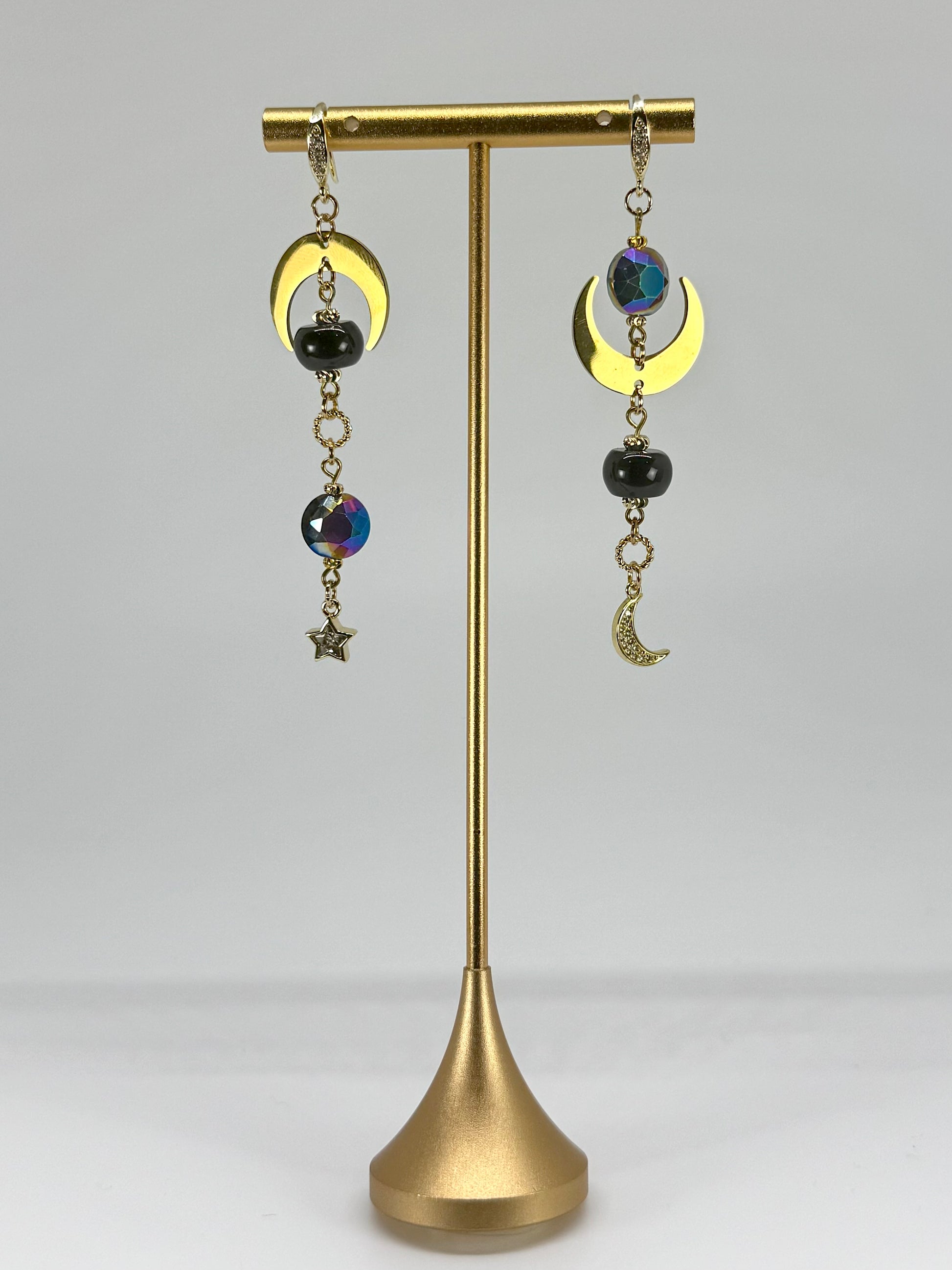 Pair of earrings on a gold stand against a gray background