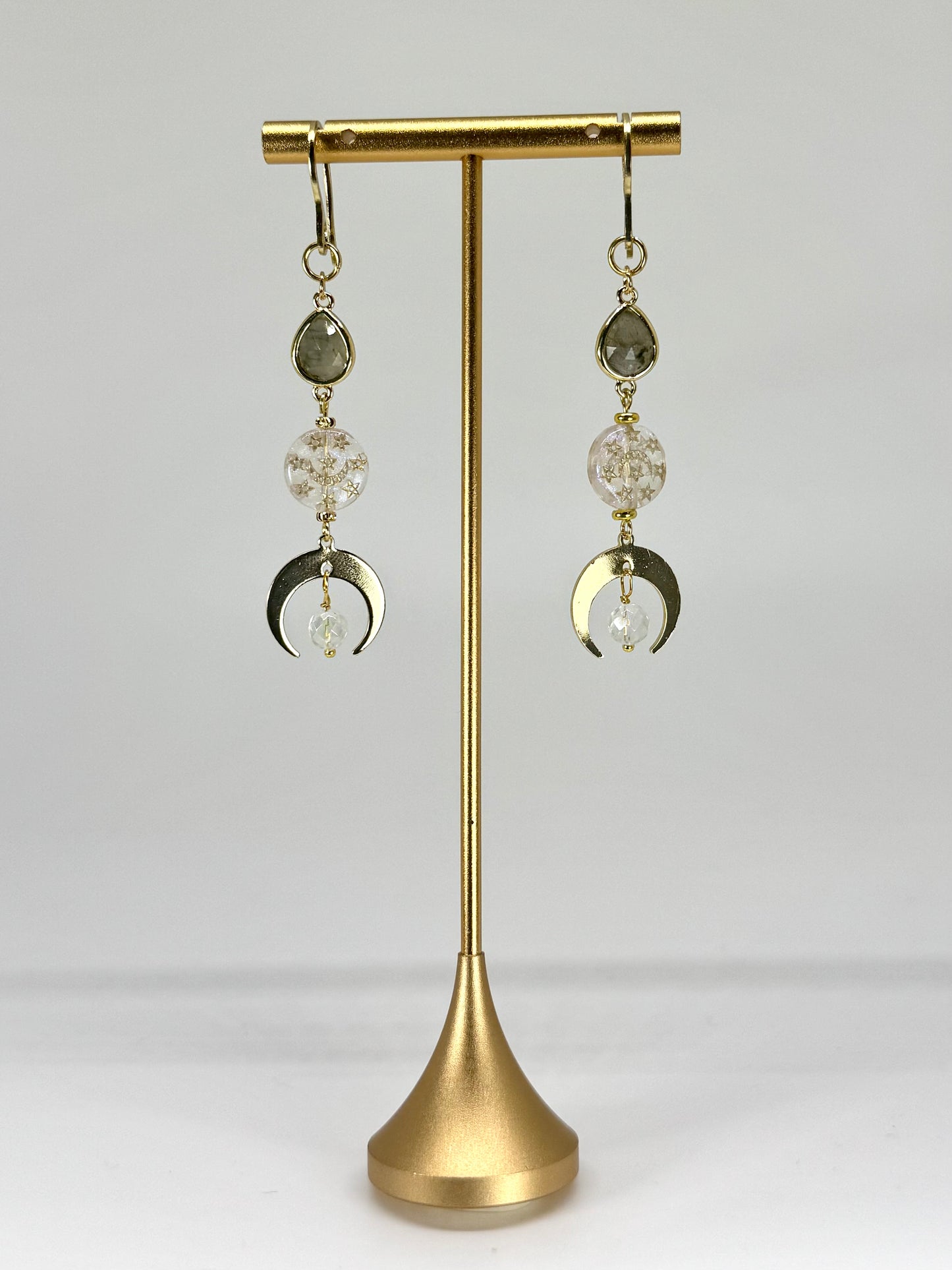Pair of earrings with crystal and moon phase design on a gold stand against a white background