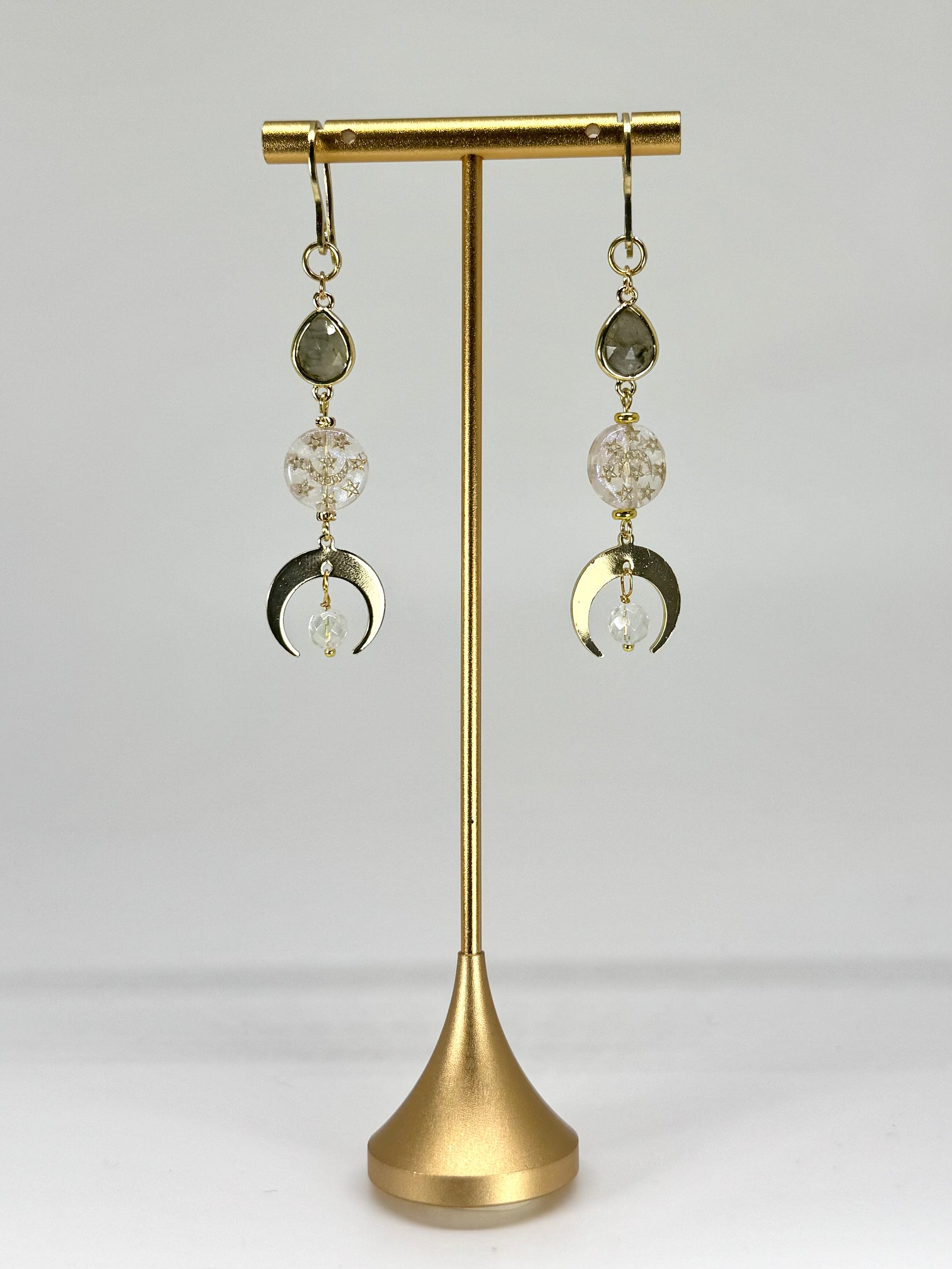 Pair of earrings with crystal and moon phase design on a gold stand against a white background