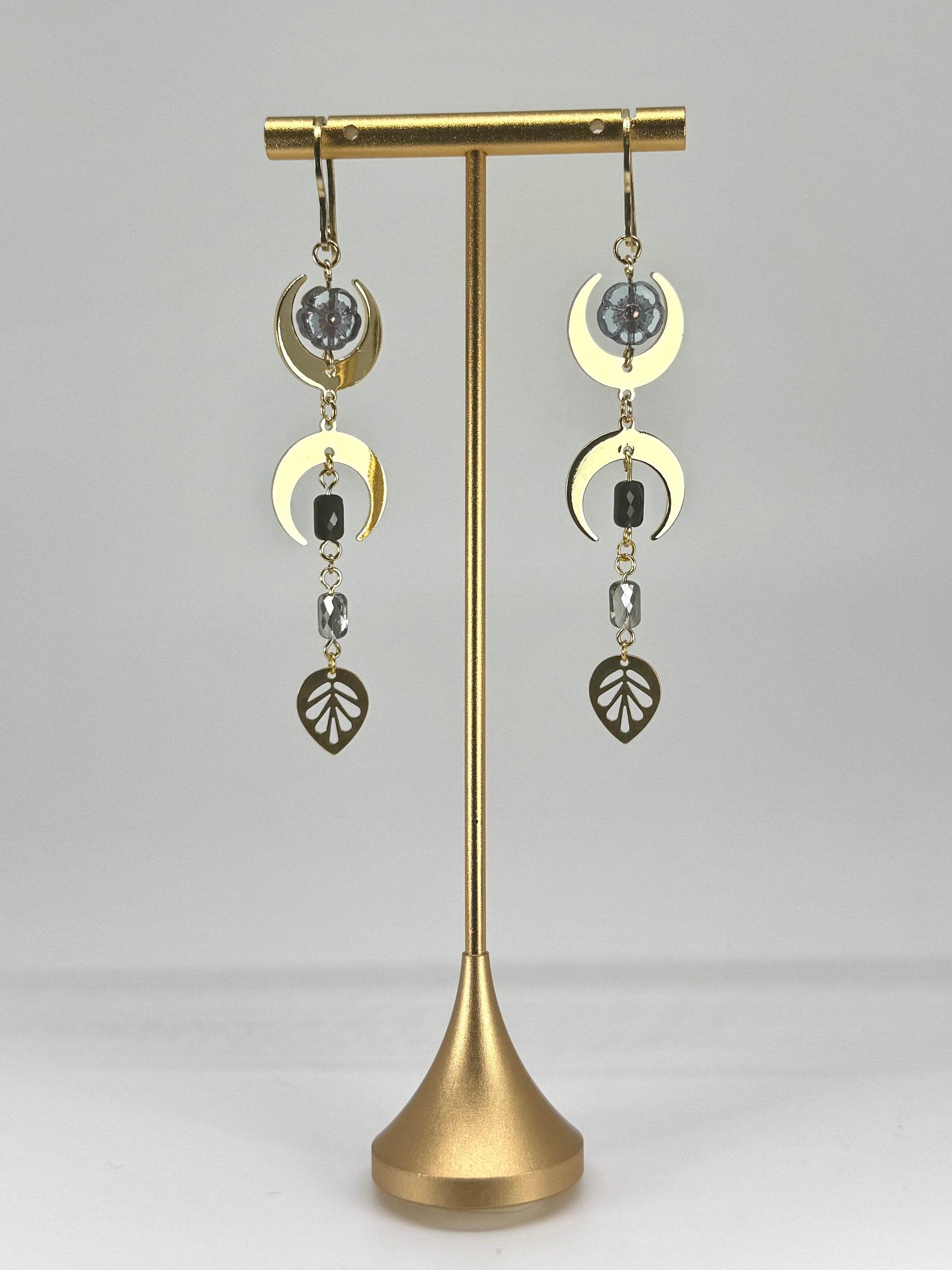 Gold earrings on a stand against a gray background