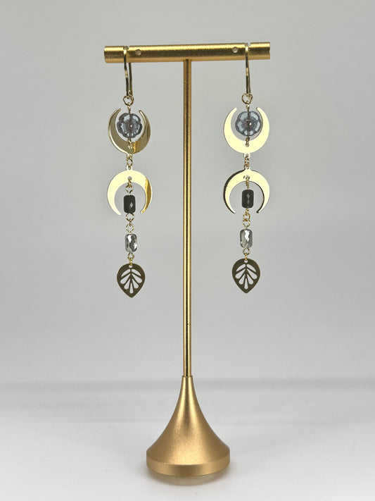 Gold earrings on a stand against a gray background