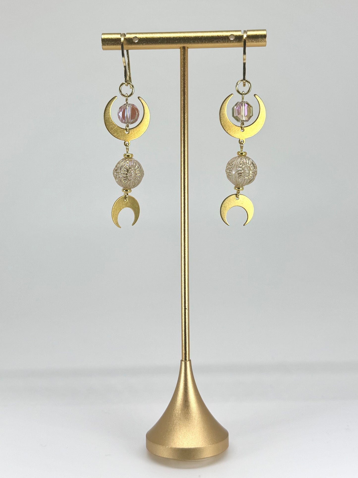 Gold earrings with spherical charms on a gold stand against a white background