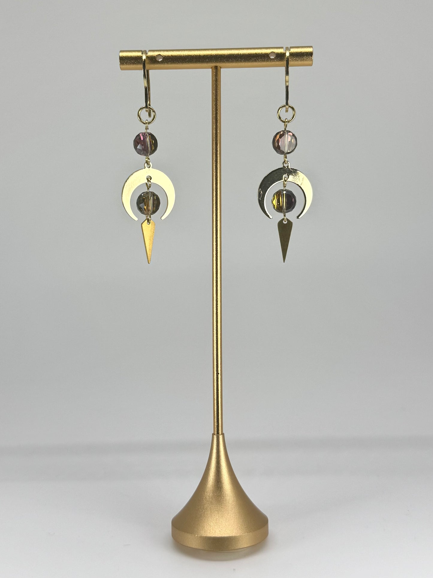 Brass earring stand with two earrings on a gray background