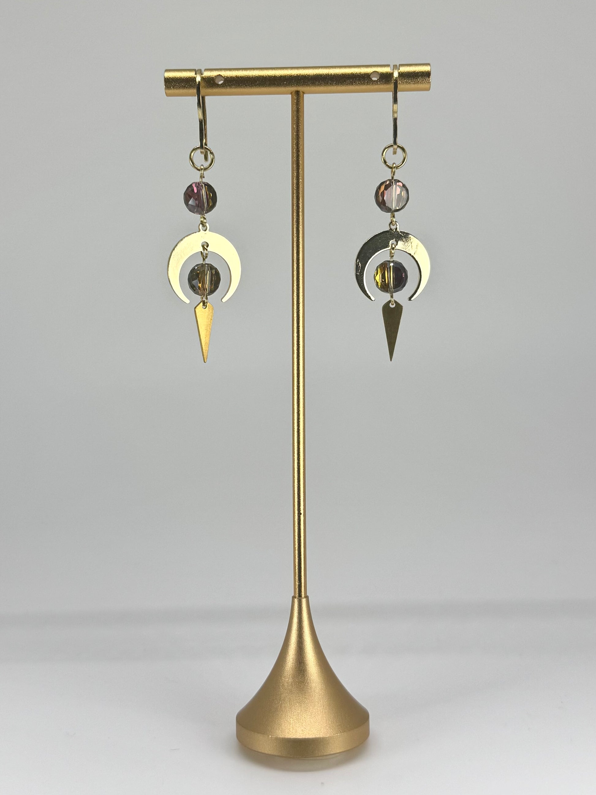 Brass earring stand with two earrings on a gray background