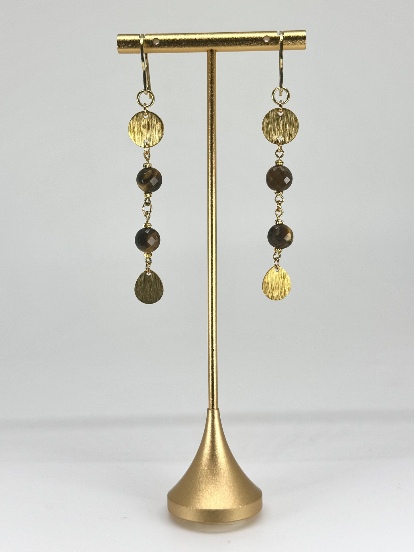 Gold and brown beaded earrings on a gold stand against a white background
