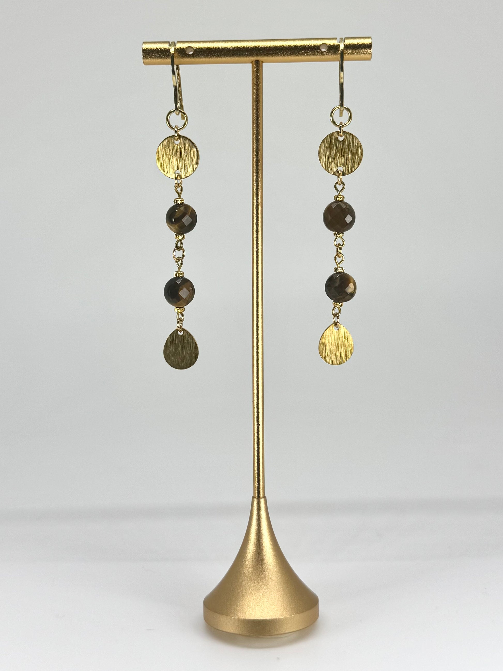 Gold and brown beaded earrings on a gold stand against a white background