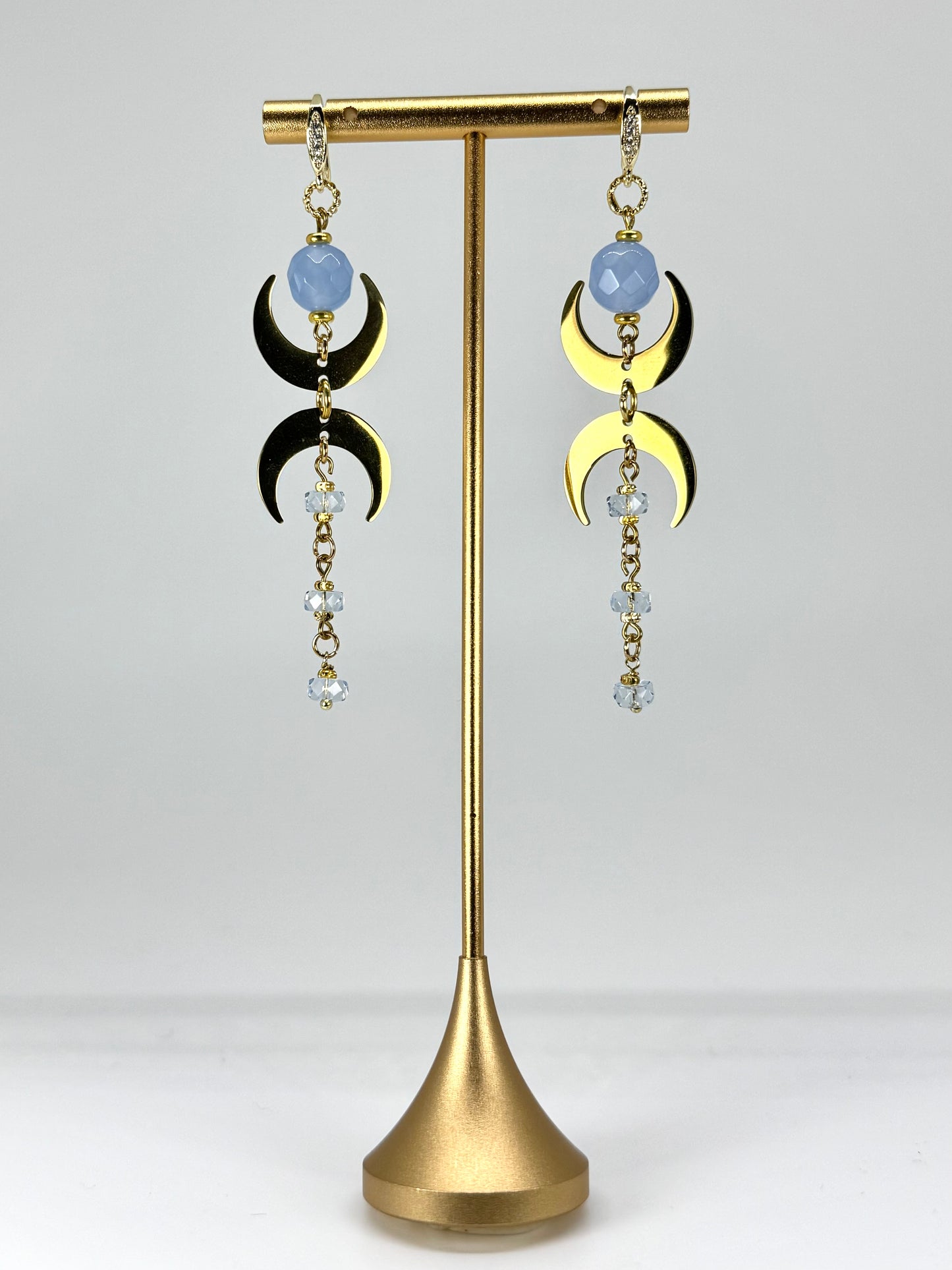 Pair of earrings with gold and black crescent moon designs on a gold stand against a white background
