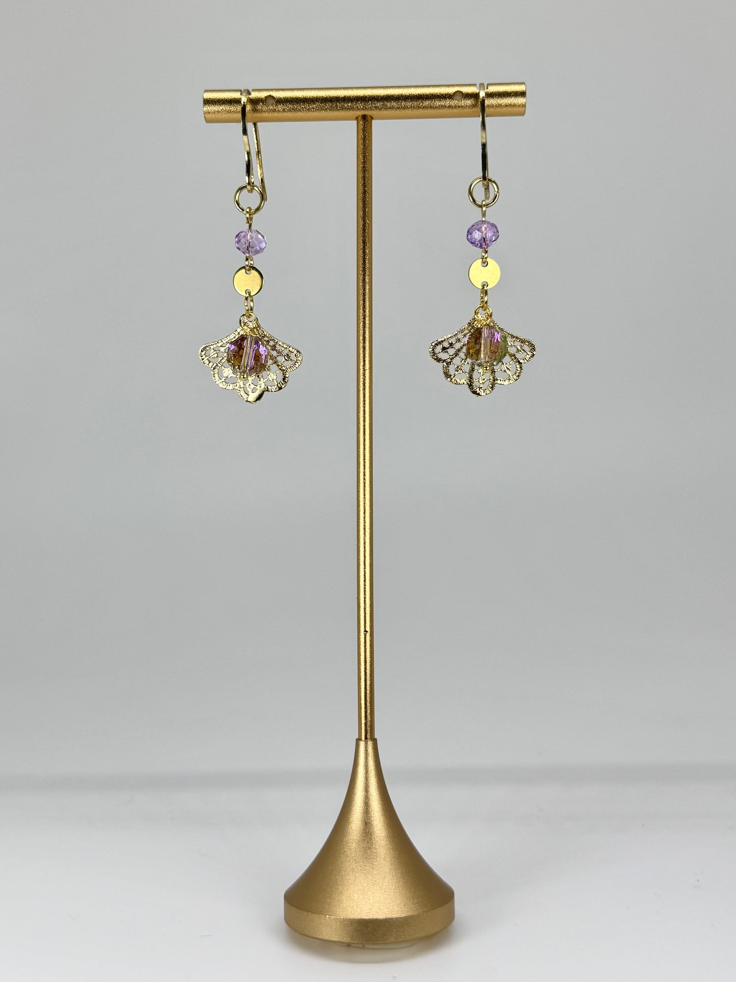 Pair of gold earrings with purple and yellow beads on a gold stand against a gray background