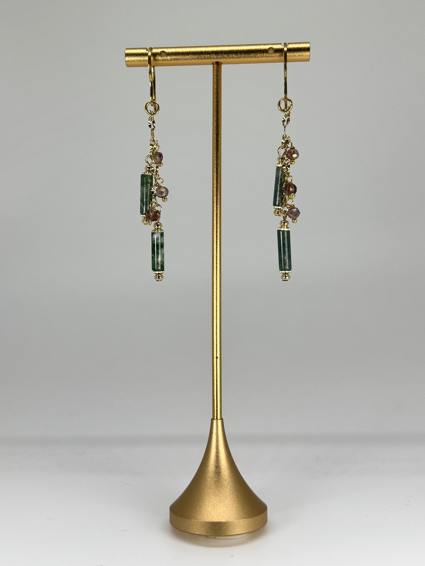 Gold earring stand with dangling earrings on a gray background