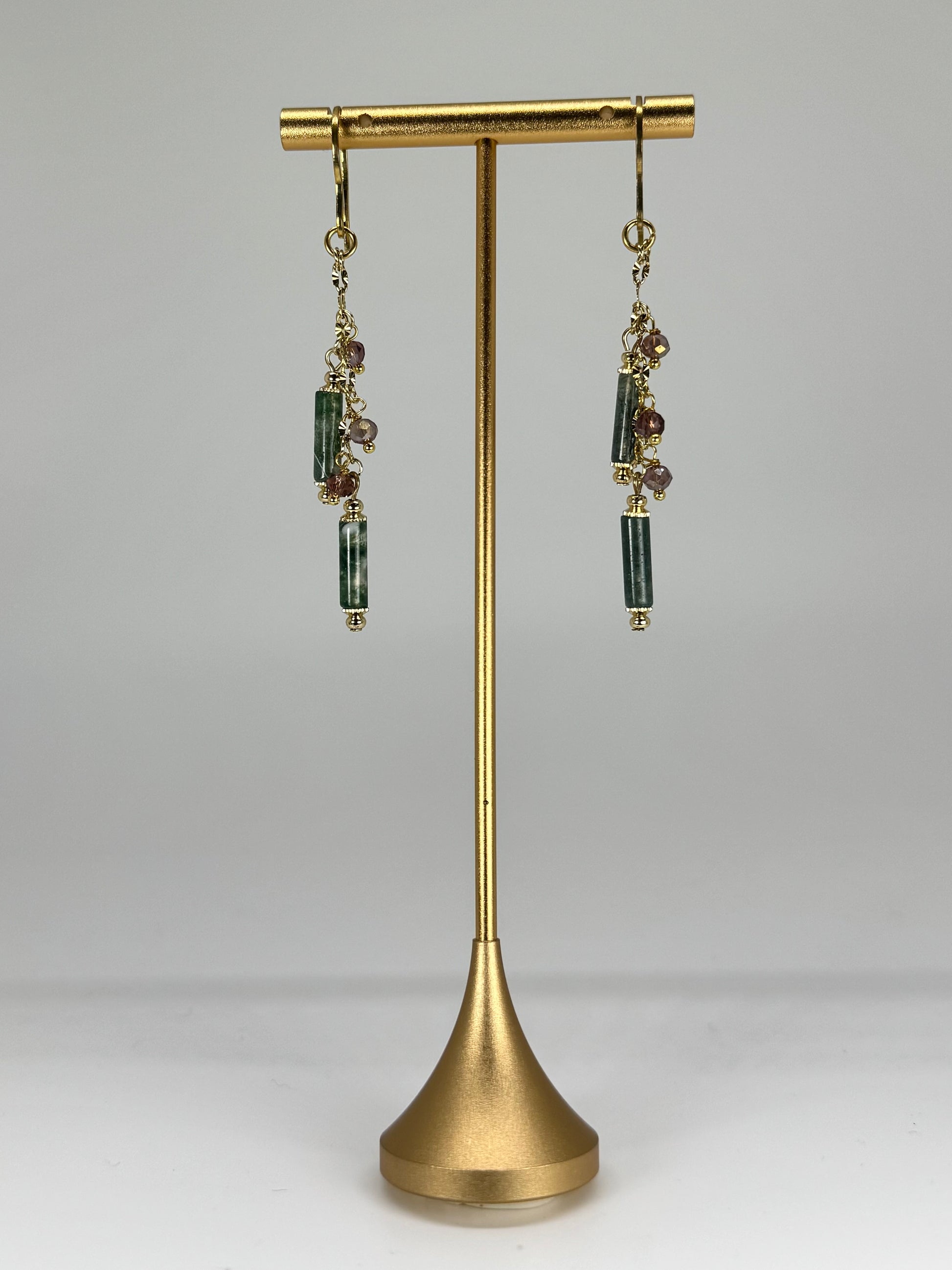 Gold earring stand with dangling earrings on a gray background