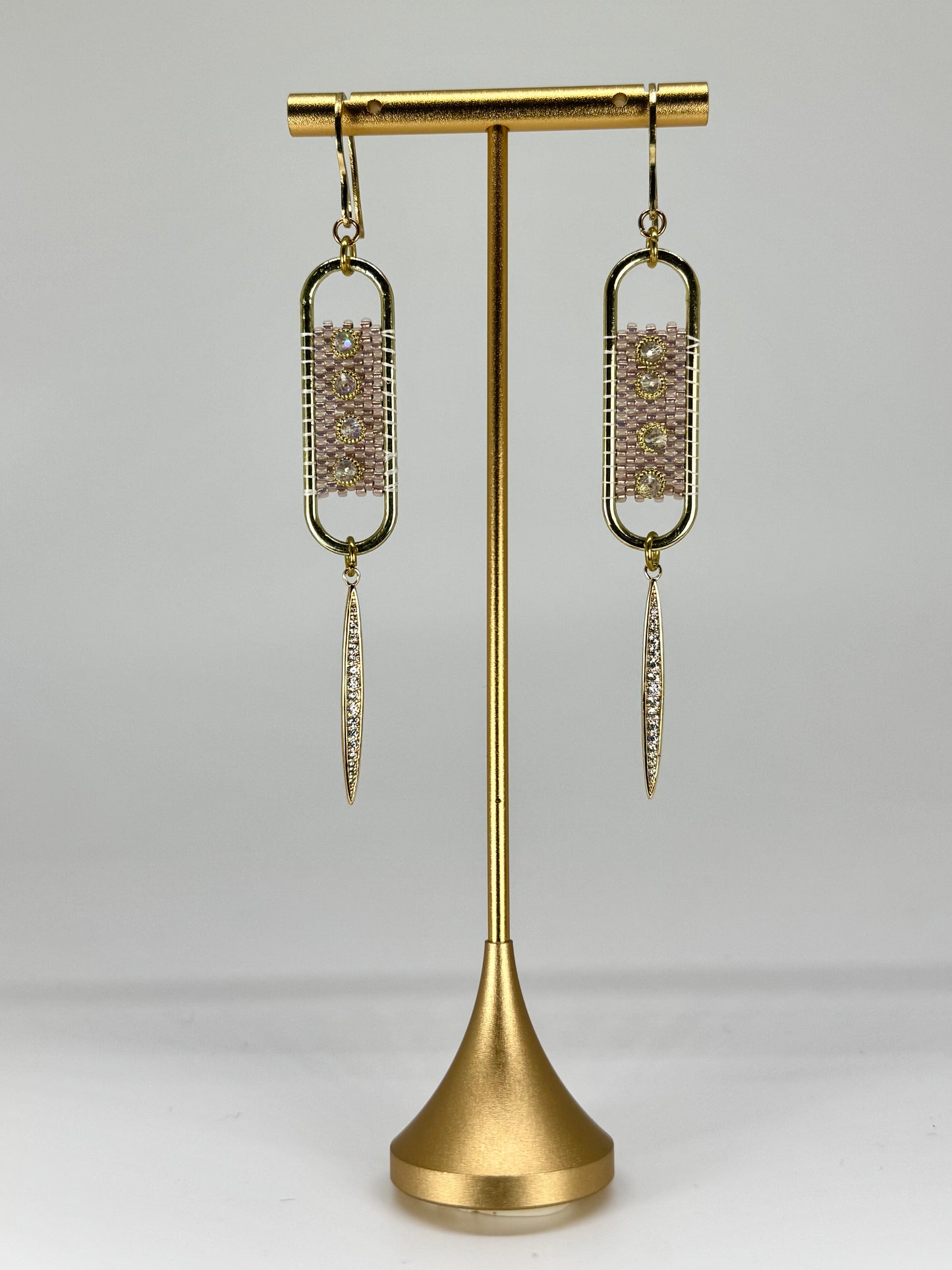 Gold earrings on a gold stand against a white background
