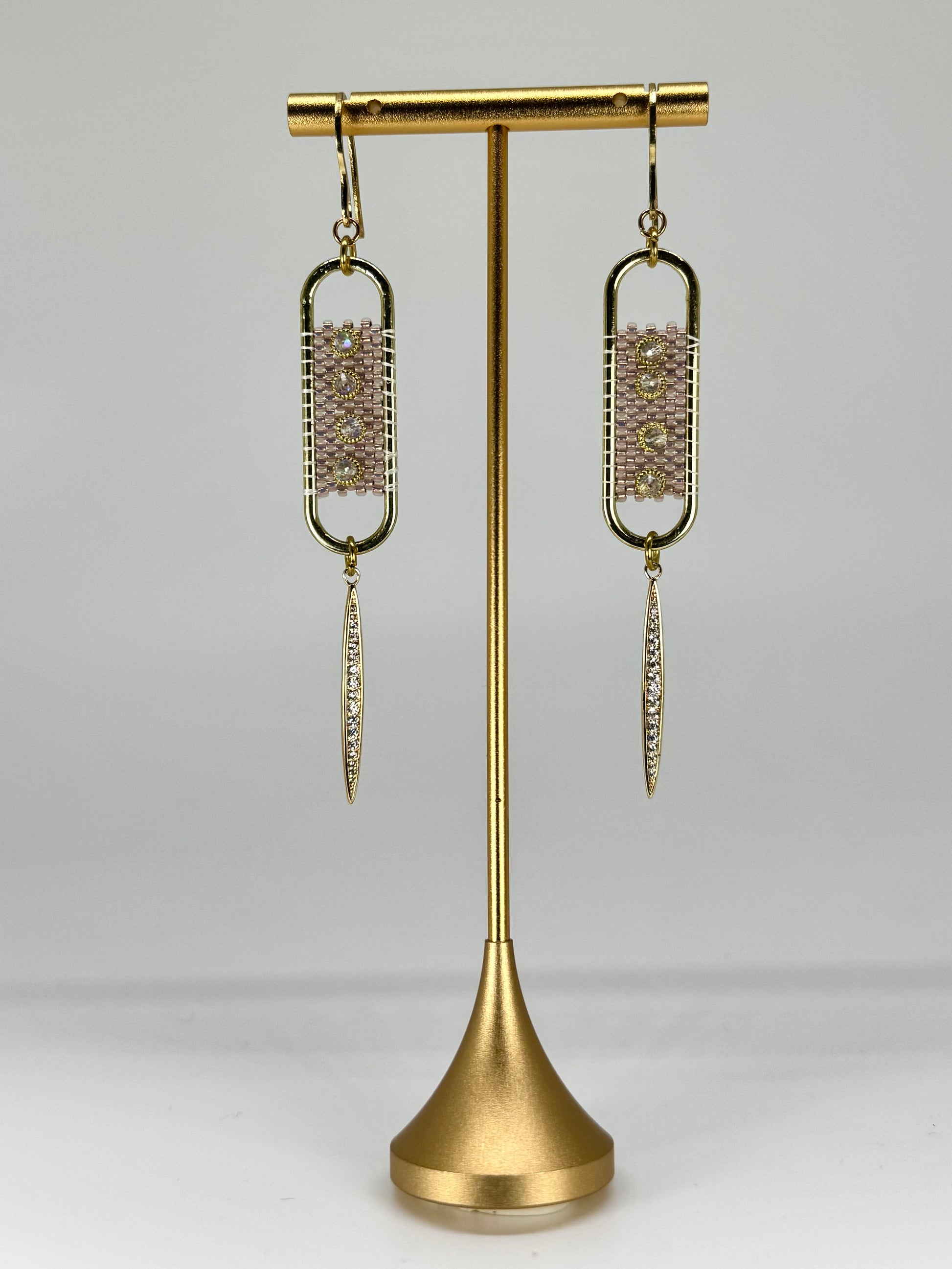 Gold earrings on a gold stand against a white background