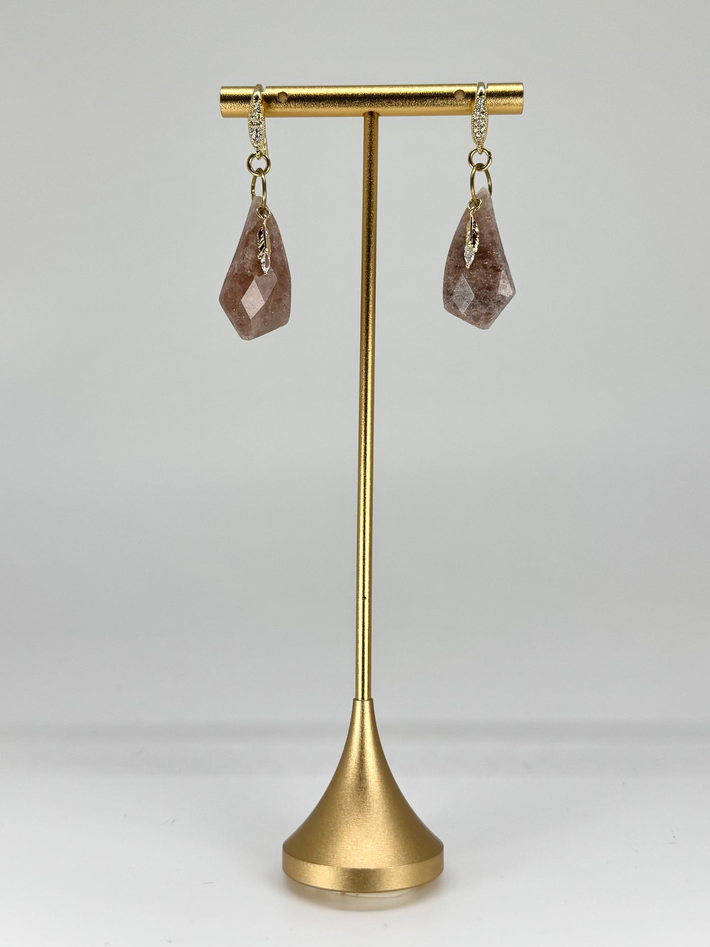 Gold earring stand with teardrop-shaped earrings on a white background