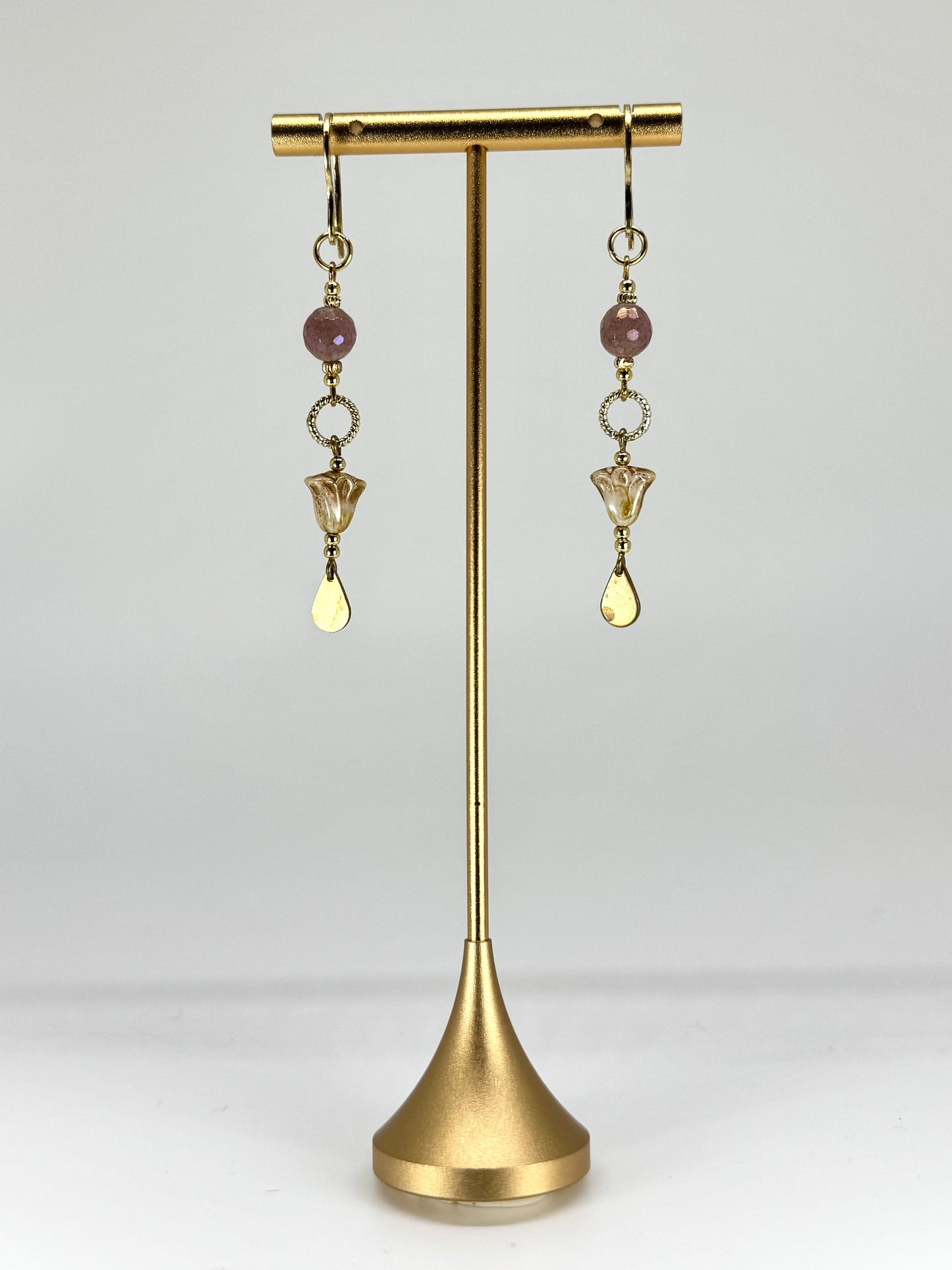 Gold earrings with beads on a gold stand against a white background