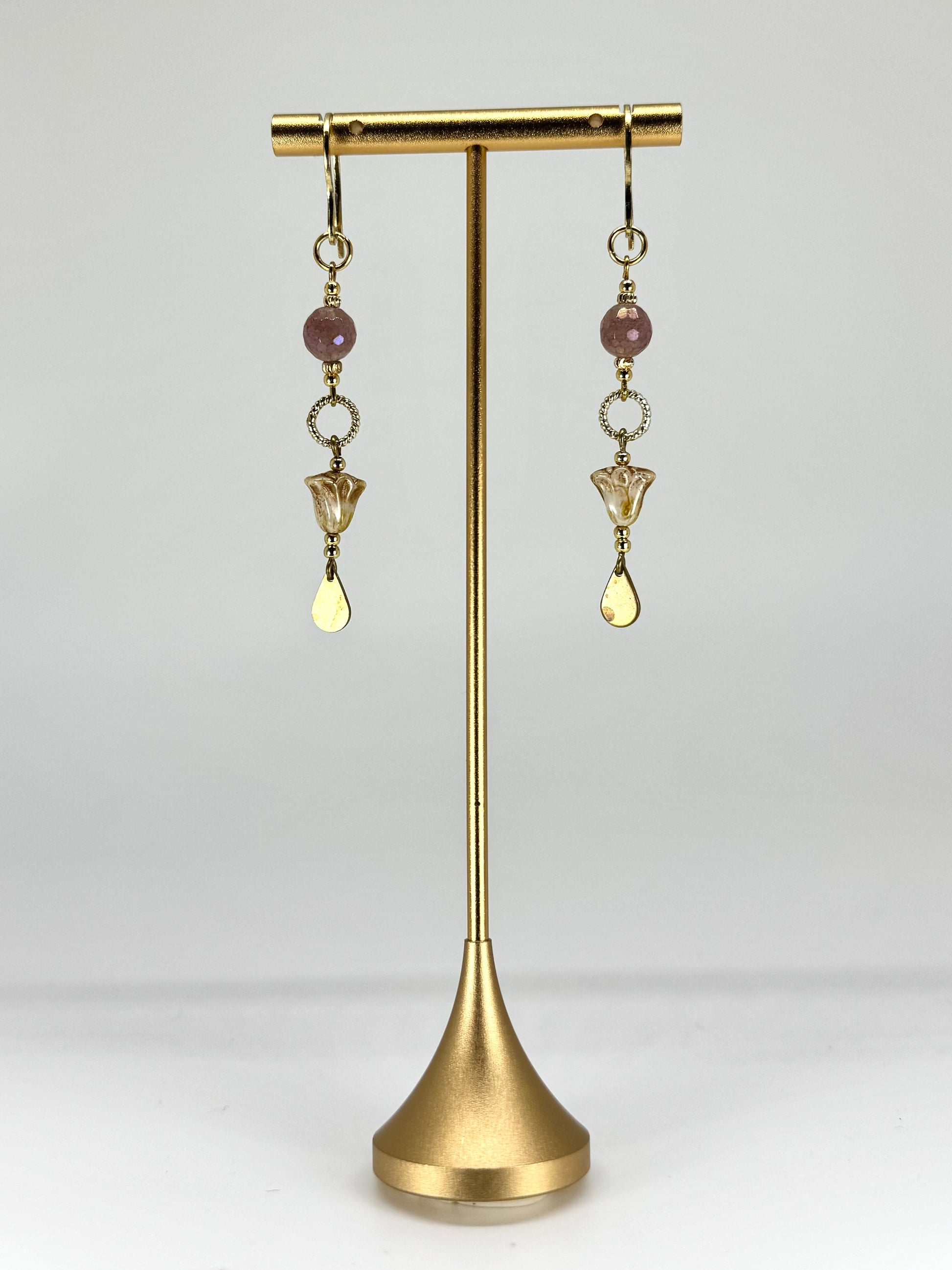 Gold earrings with beads on a gold stand against a white background