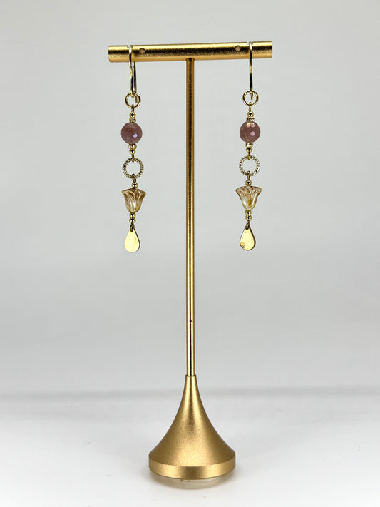 Gold earrings with beads on a gold stand against a white background