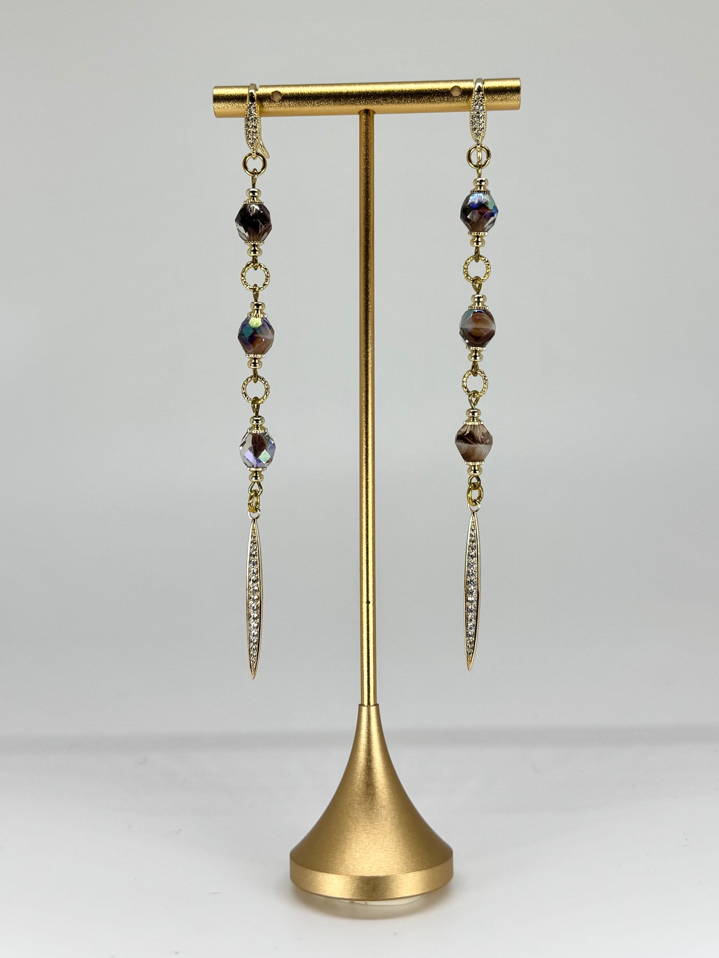 Pair of dangling earrings on a gold stand against a white background