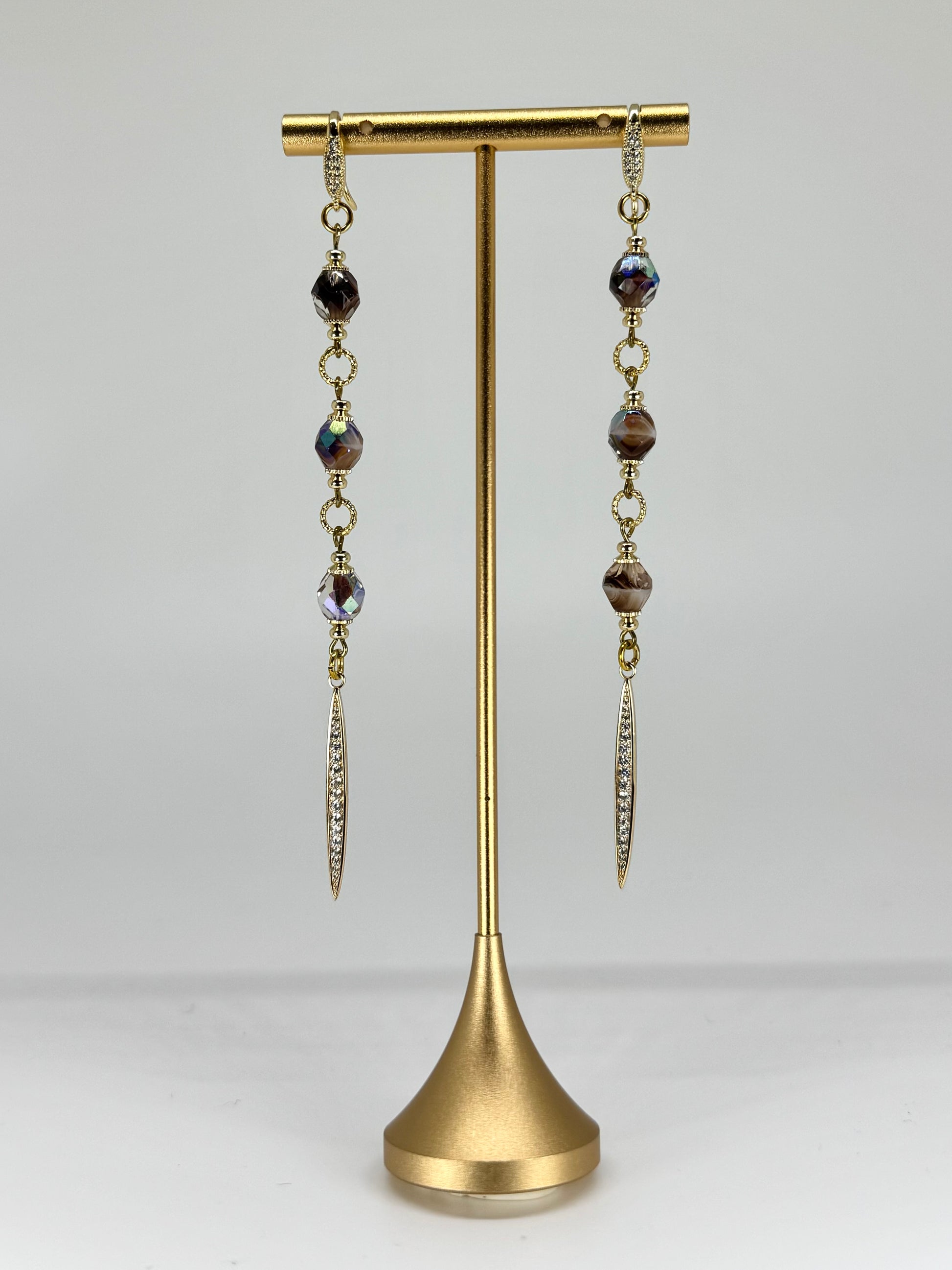 Pair of dangling earrings on a gold stand against a white background