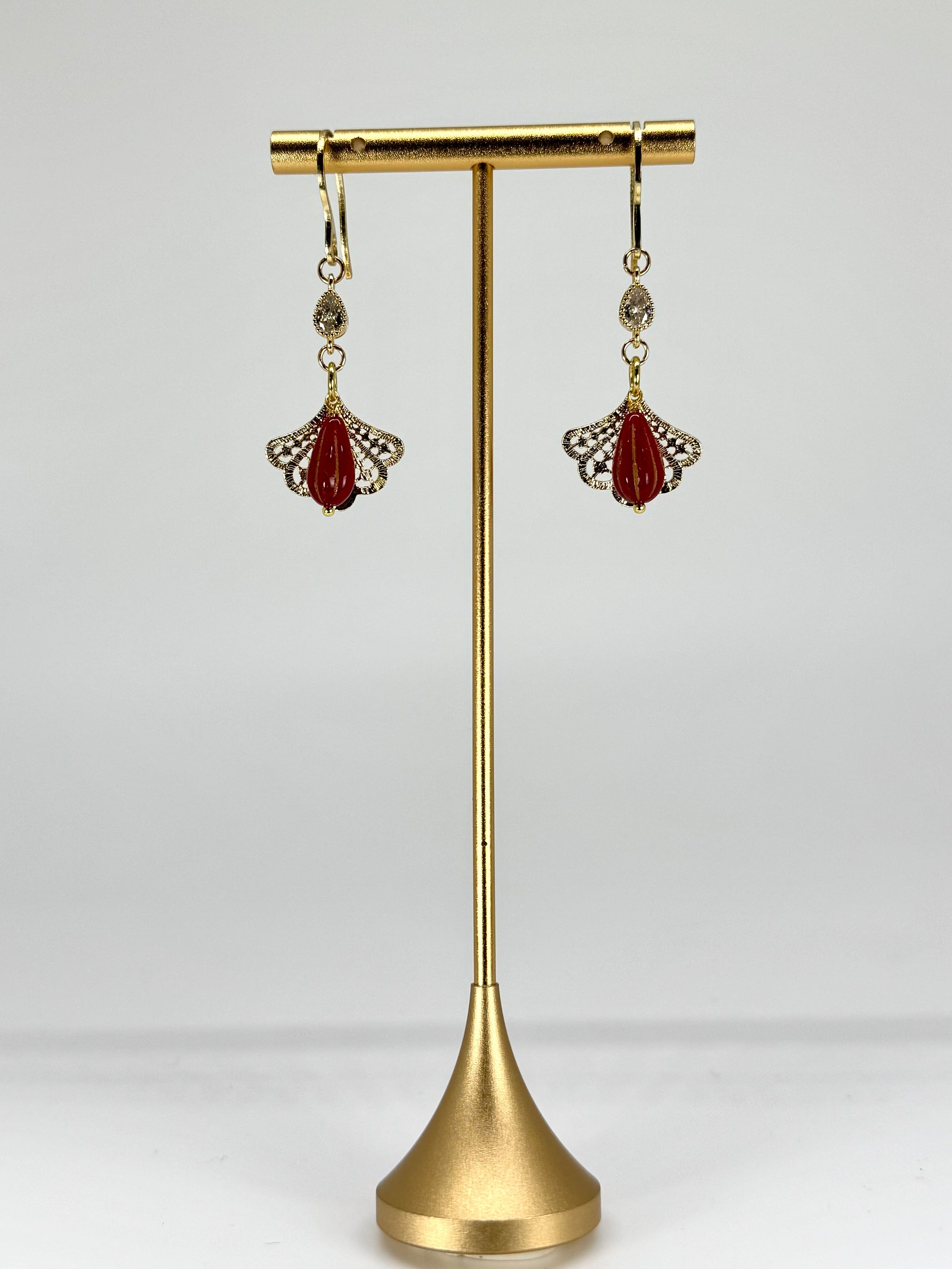 Gold earring stand with red earrings on a white background