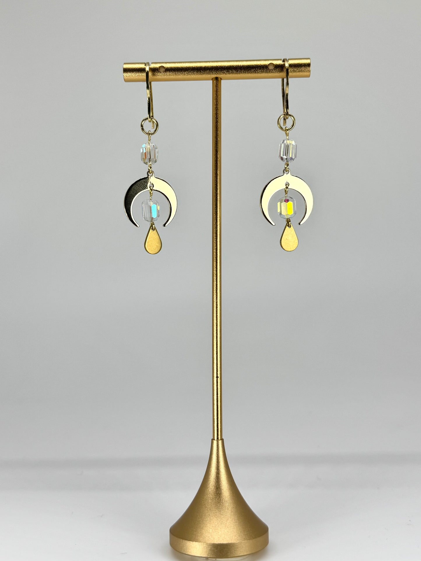 Gold earrings on a stand against a gray background