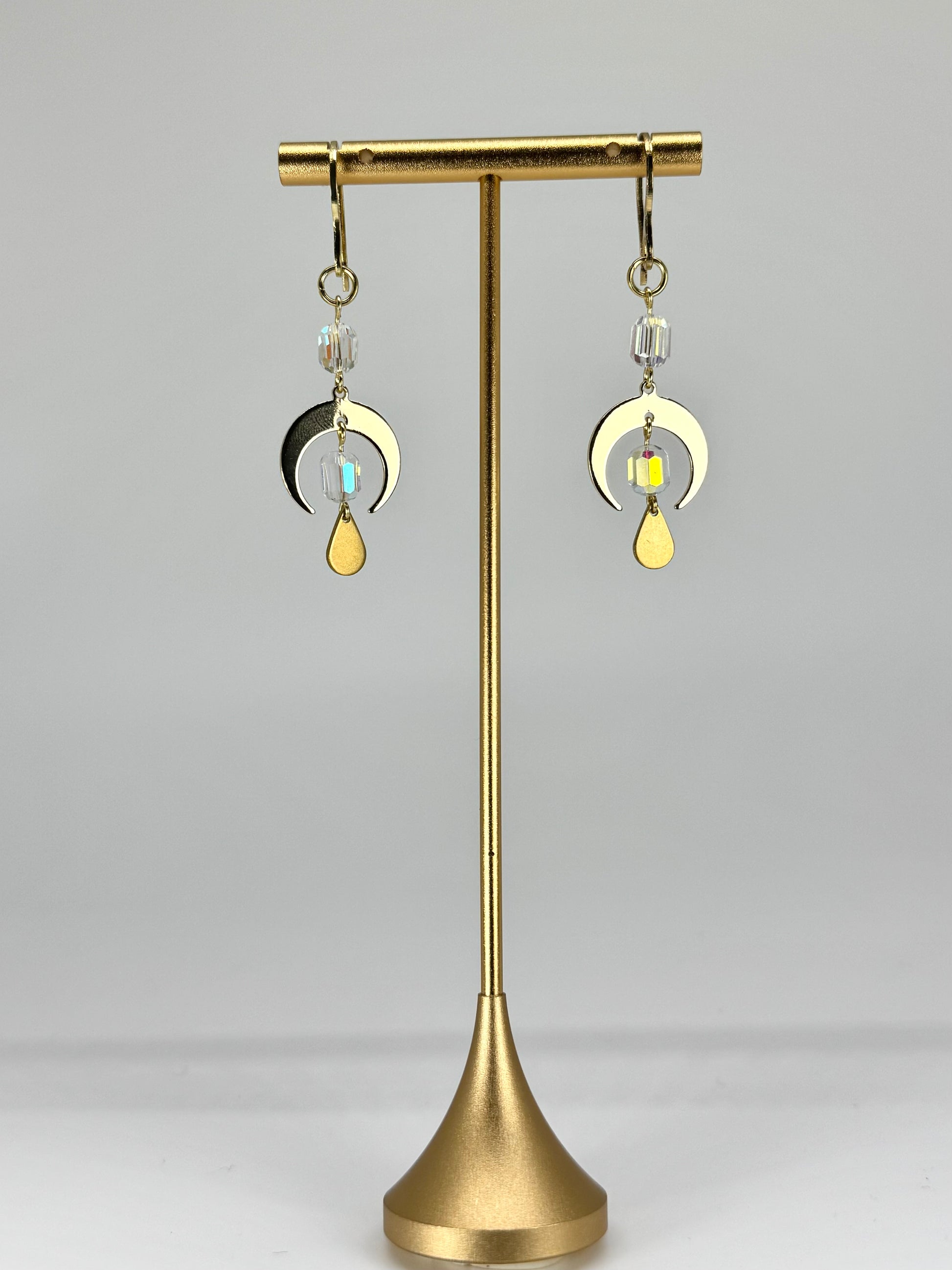 Gold earrings on a stand against a gray background