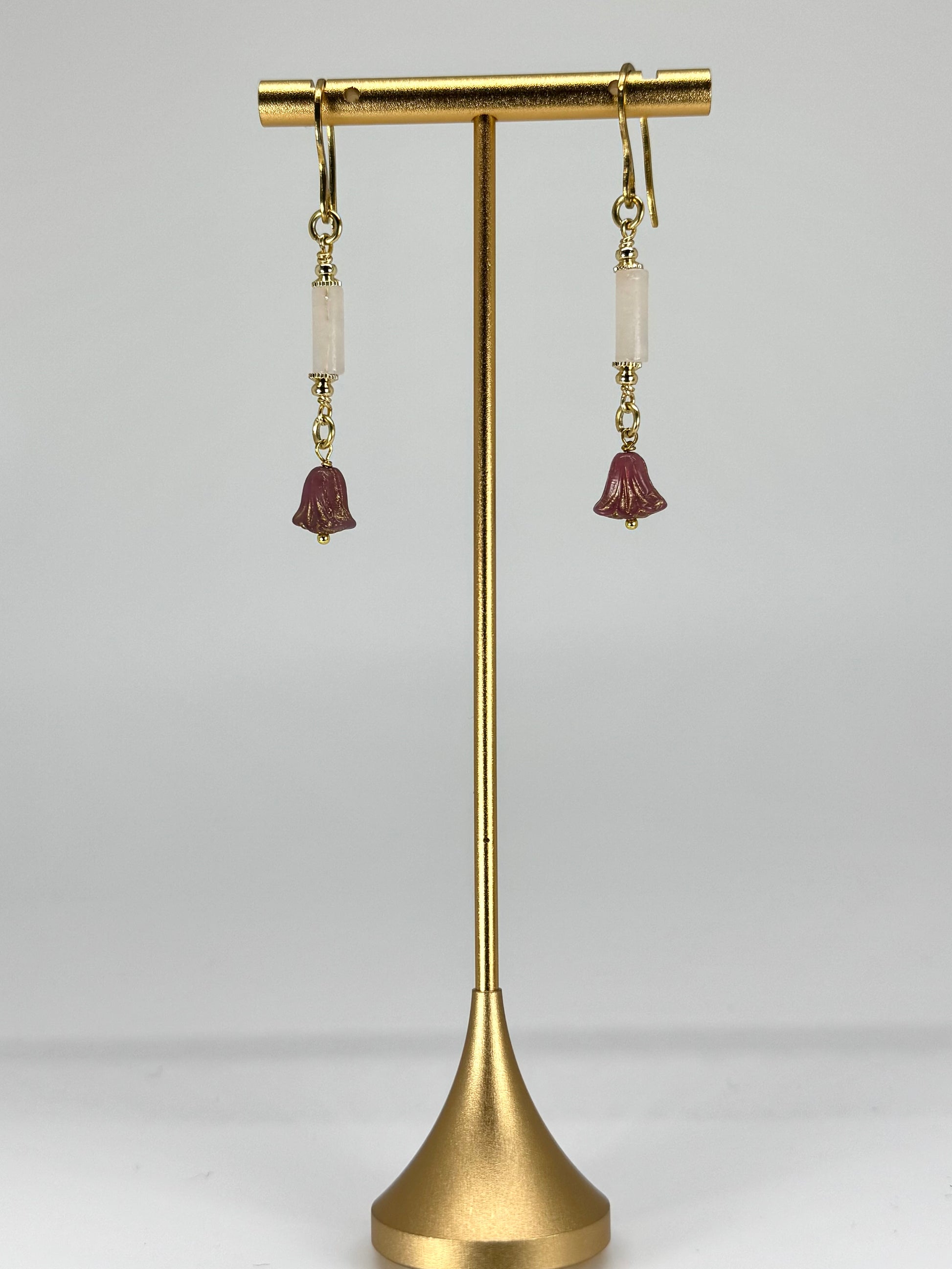 Pair of earrings on a gold stand against a white background