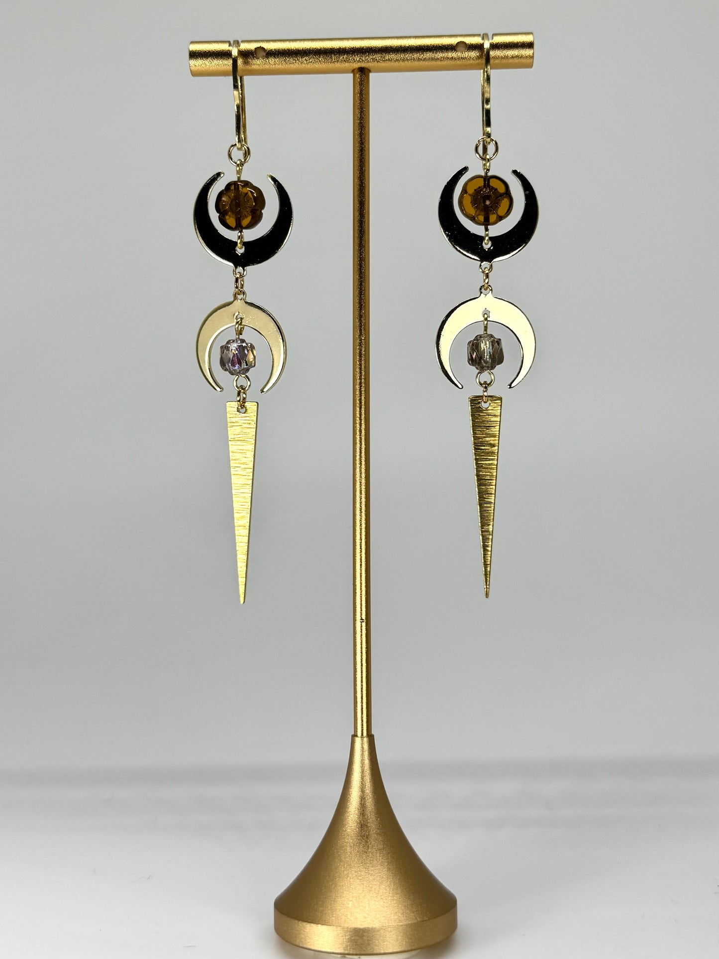 Pair of gold and black earrings on a gold stand against a gray background
