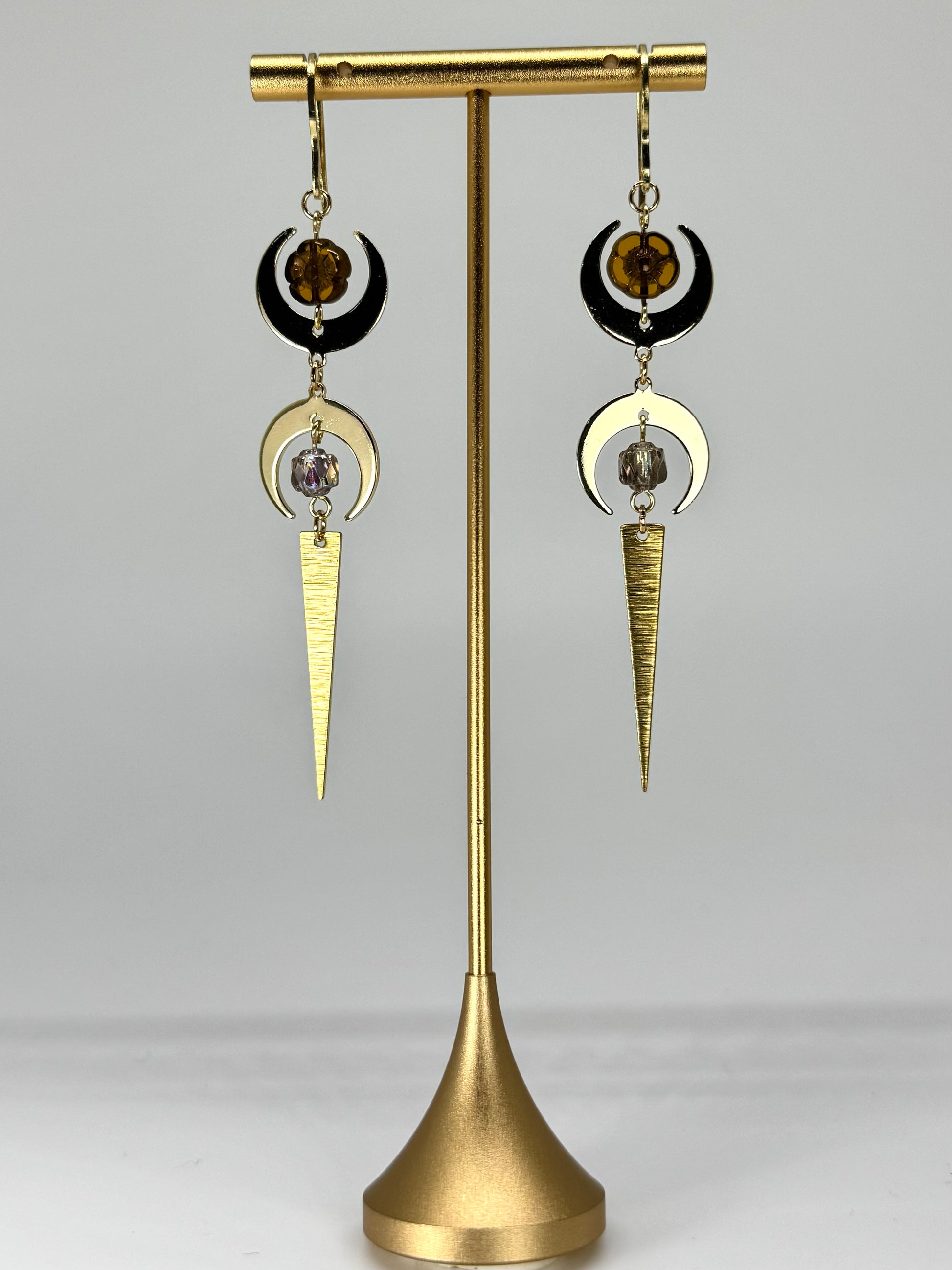 Pair of gold and black earrings on a gold stand against a gray background