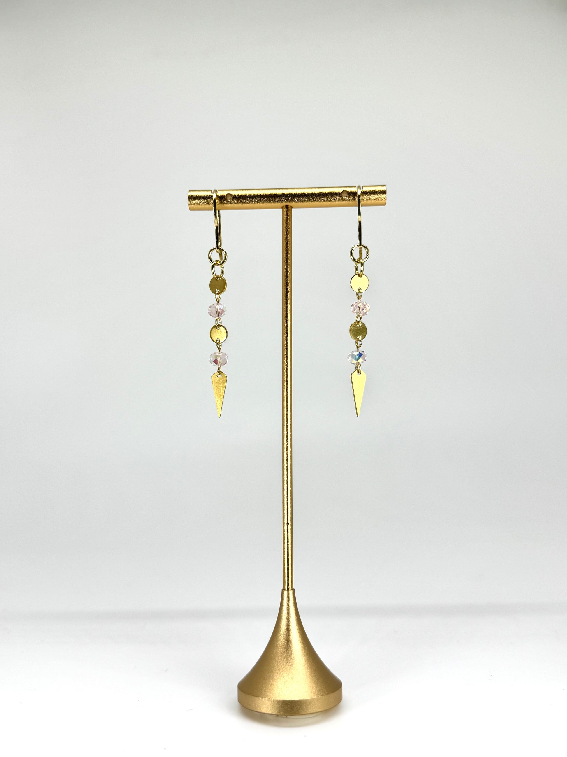 Gold earrings with dangling elements on a gold stand against a white background