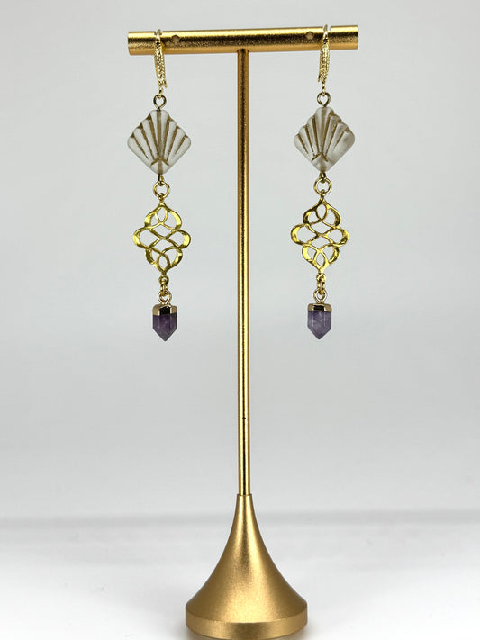 Gold earrings with purple stones on a gold stand against a white background