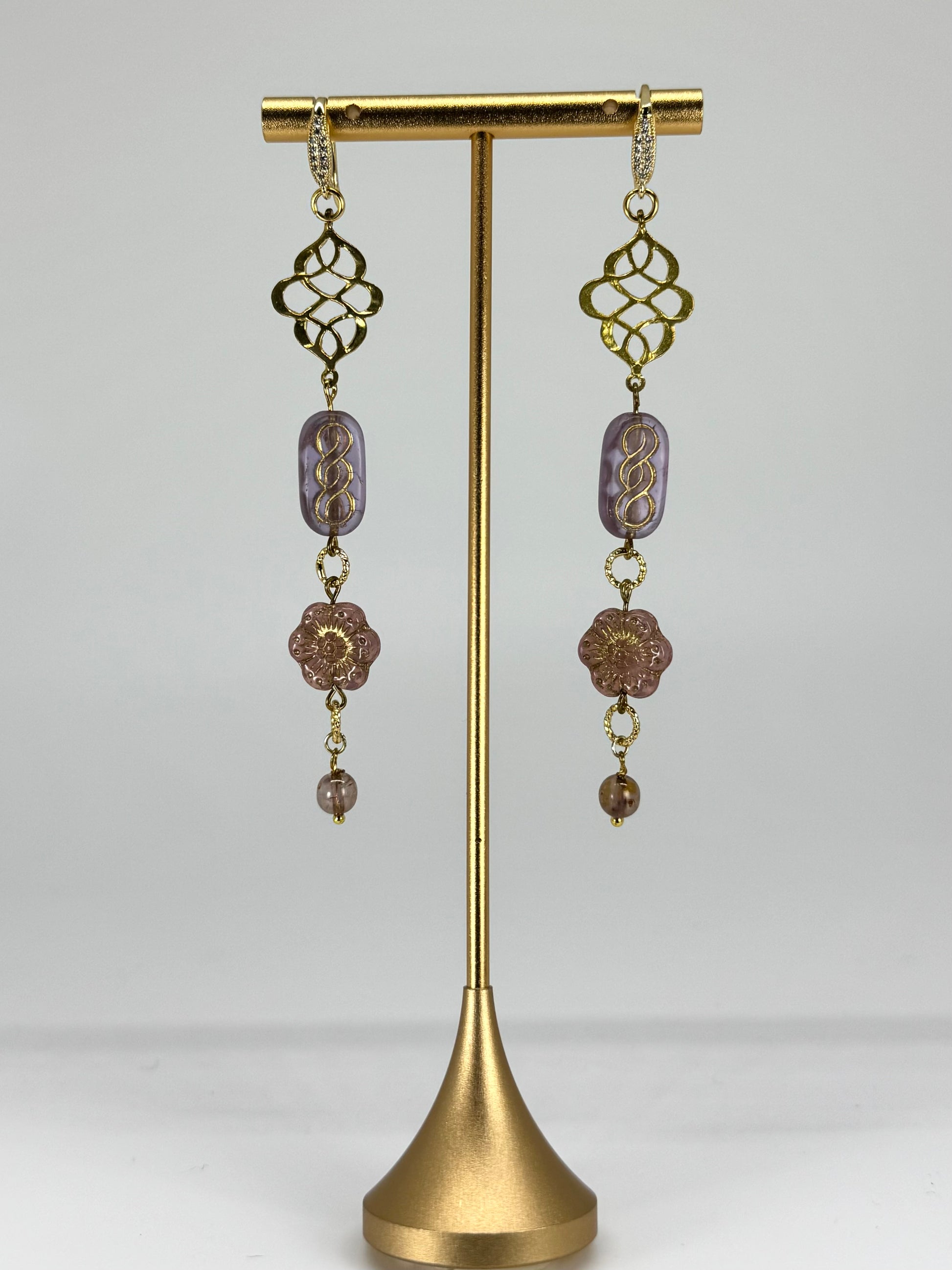 Pair of gold and purple beaded earrings on a gold stand against a white background