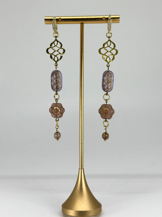 Pair of gold and purple beaded earrings on a gold stand against a white background