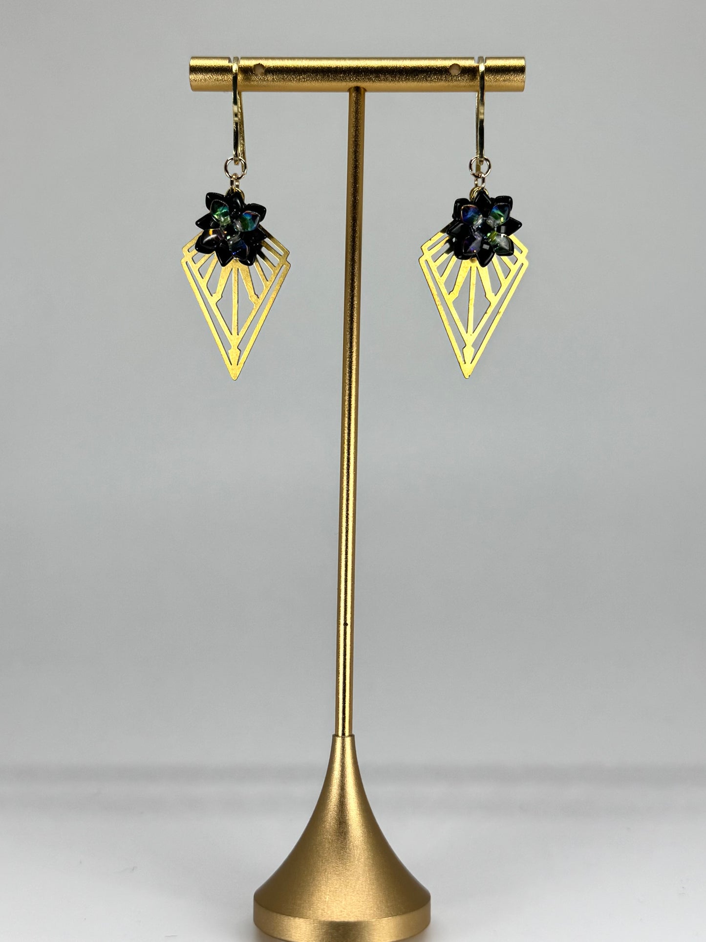 Gold earring stand with two black gemstone earrings on a white background