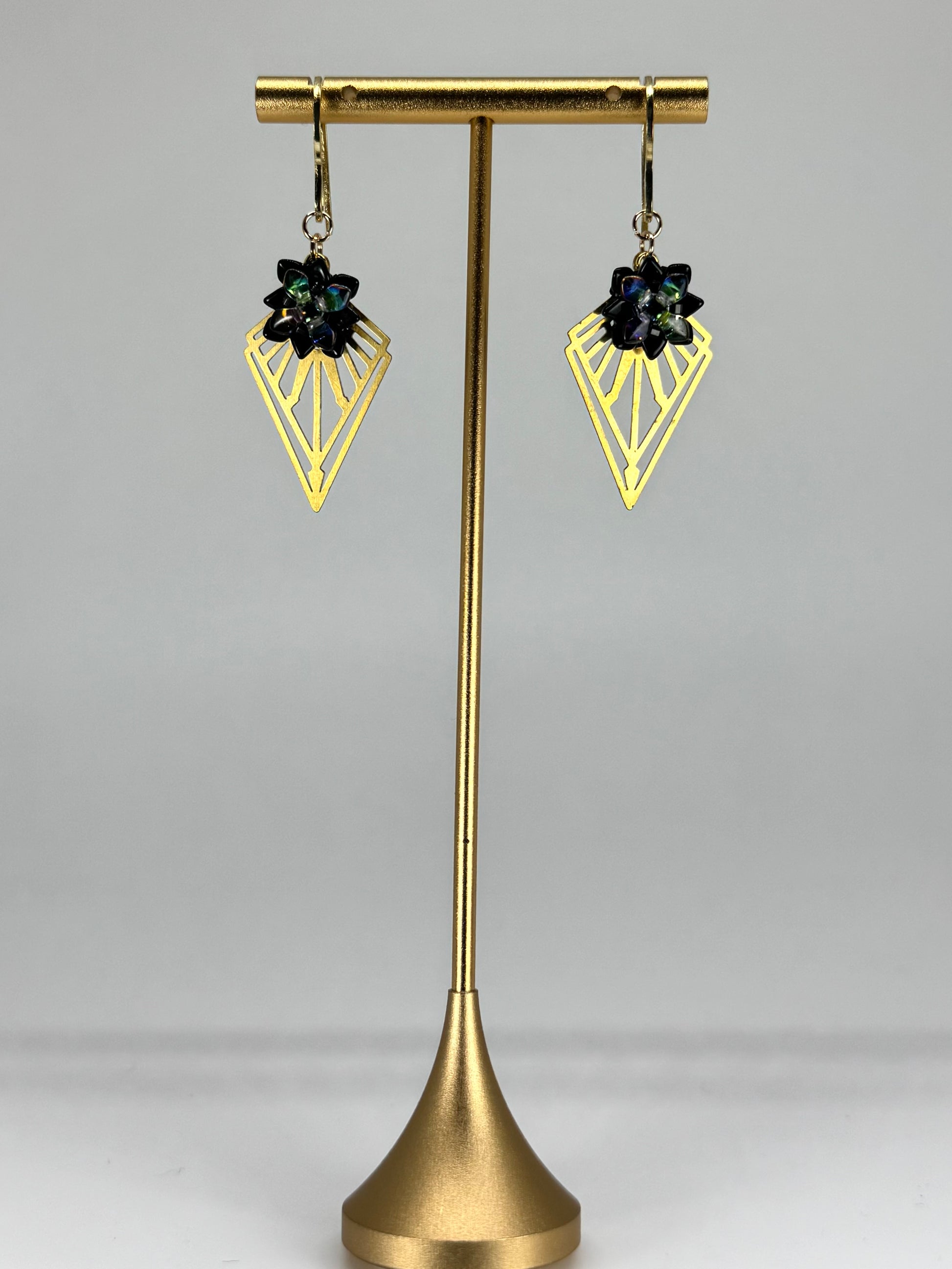 Gold earring stand with two black gemstone earrings on a white background