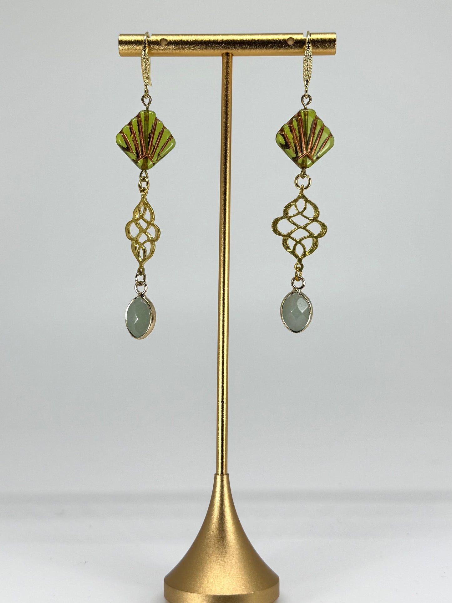 Gold earrings with green gemstones on a gold stand against a white background