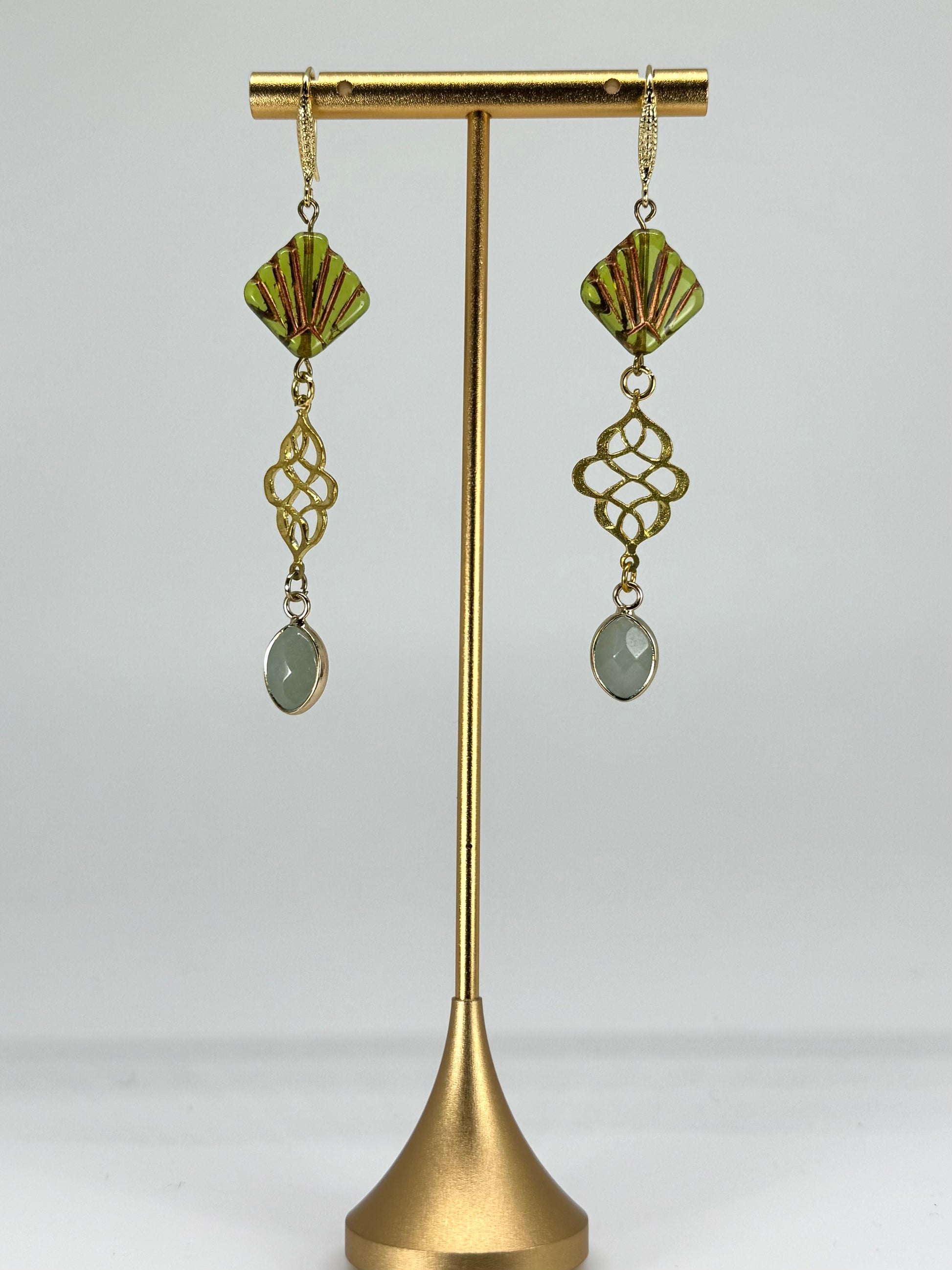 Gold earrings with green gemstones on a gold stand against a white background