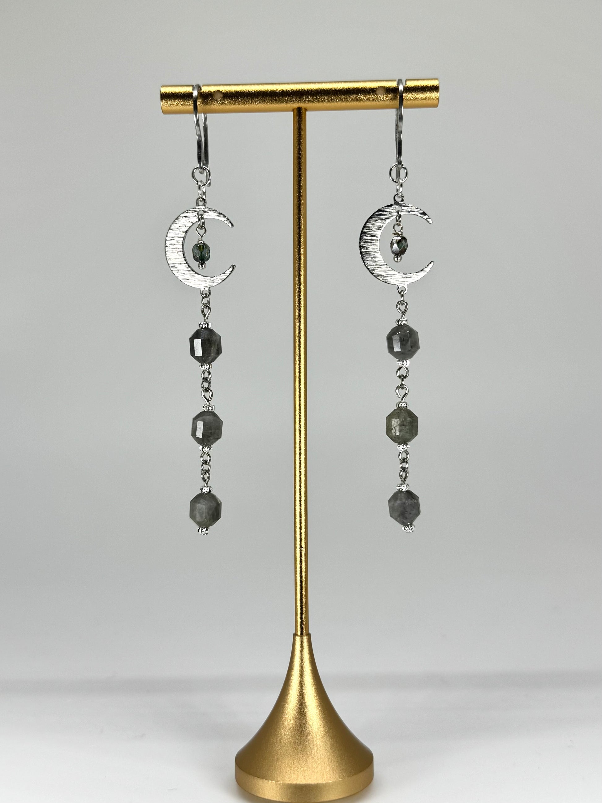Pair of earrings with moon designs on a gold stand against a gray background