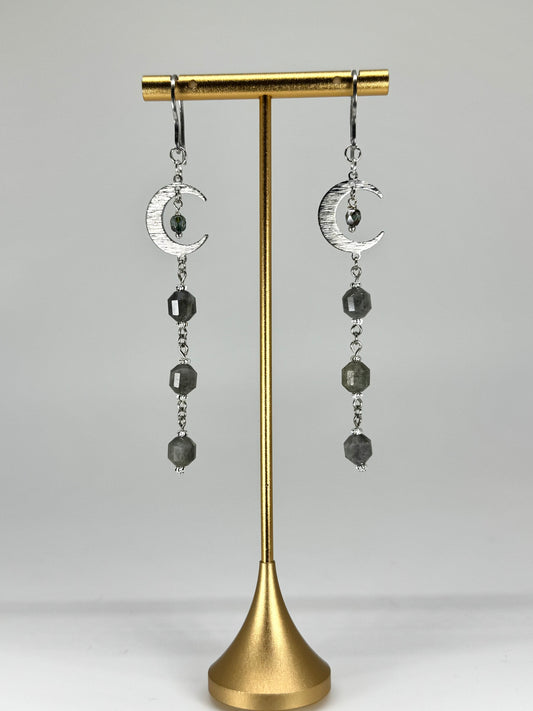 Pair of earrings with moon designs on a gold stand against a gray background