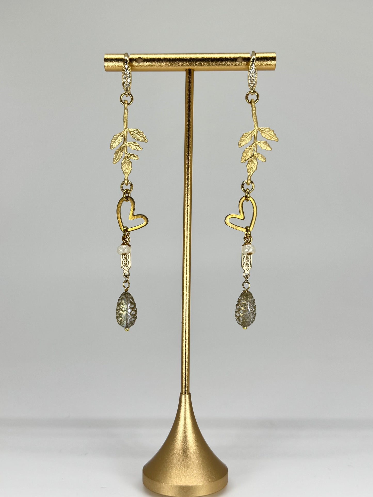 Gold heart-shaped earrings on a gold stand against a gray background