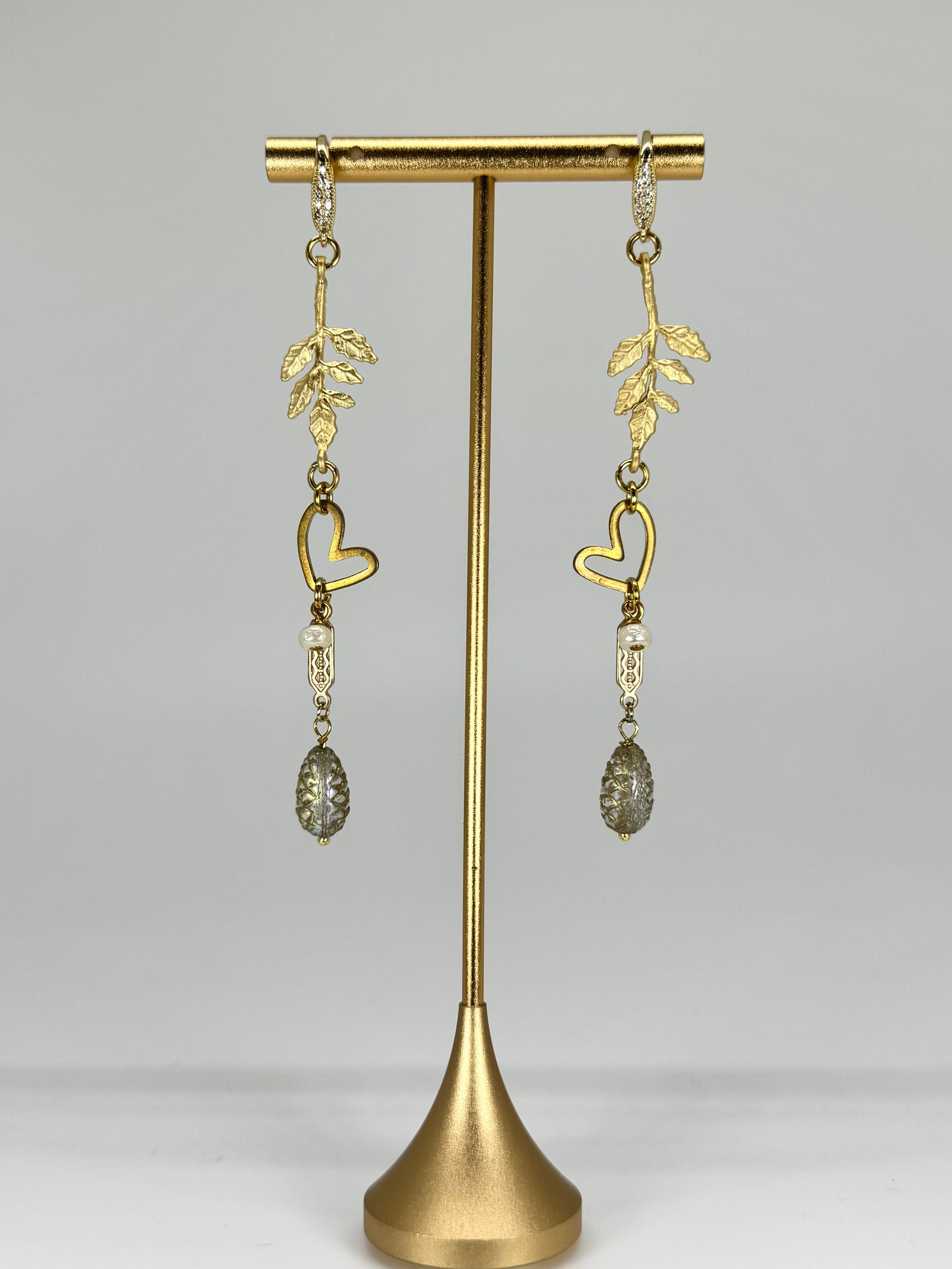 Gold heart-shaped earrings on a gold stand against a gray background
