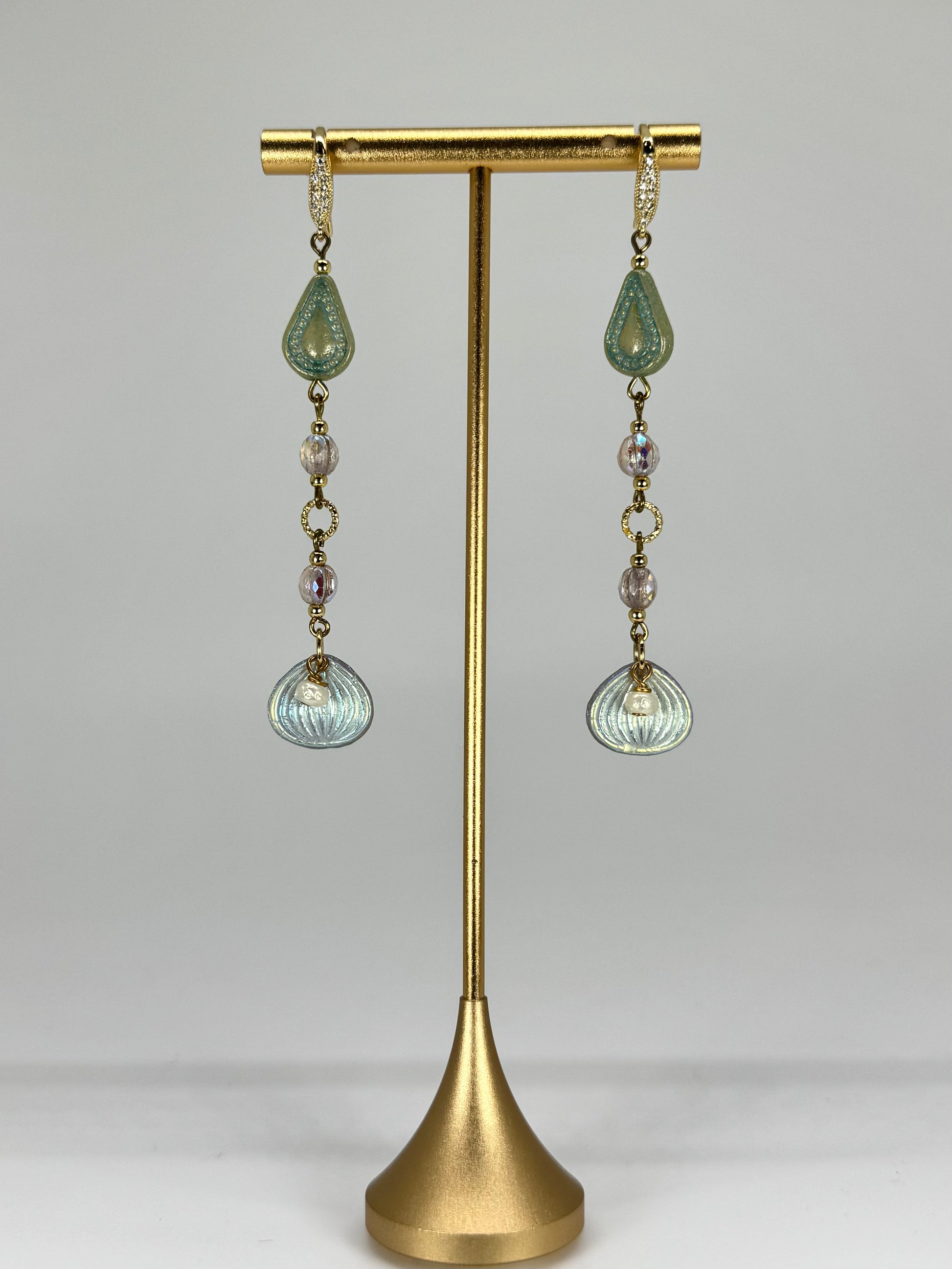 Pair of earrings with green and clear glass drops on a gold stand against a gray background