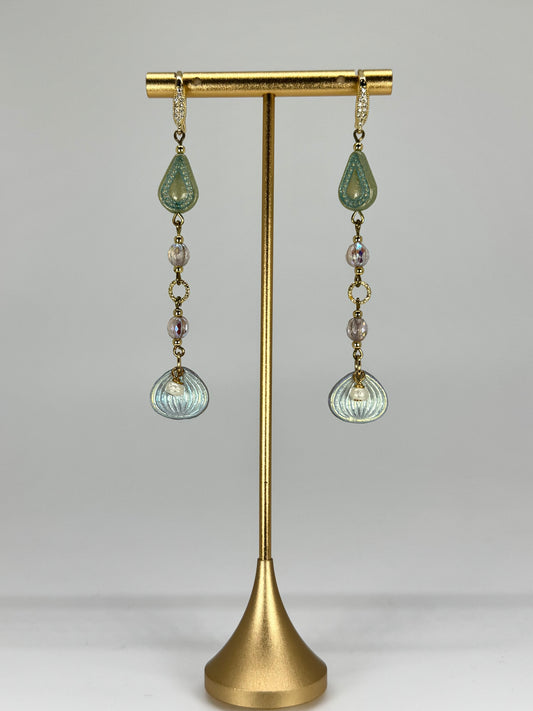 Pair of earrings with green and clear glass drops on a gold stand against a gray background