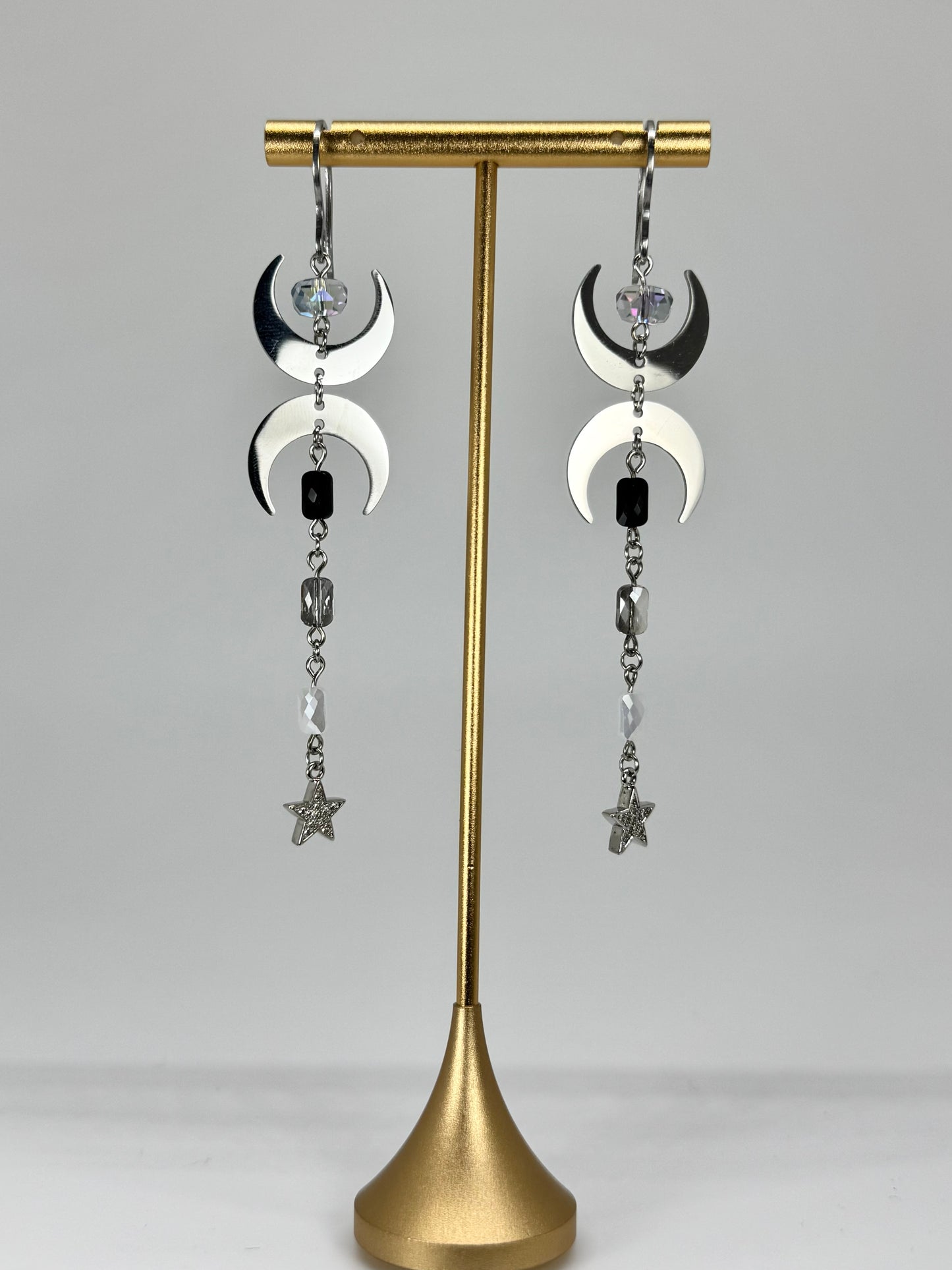 Pair of earrings on a gold stand against a gray background