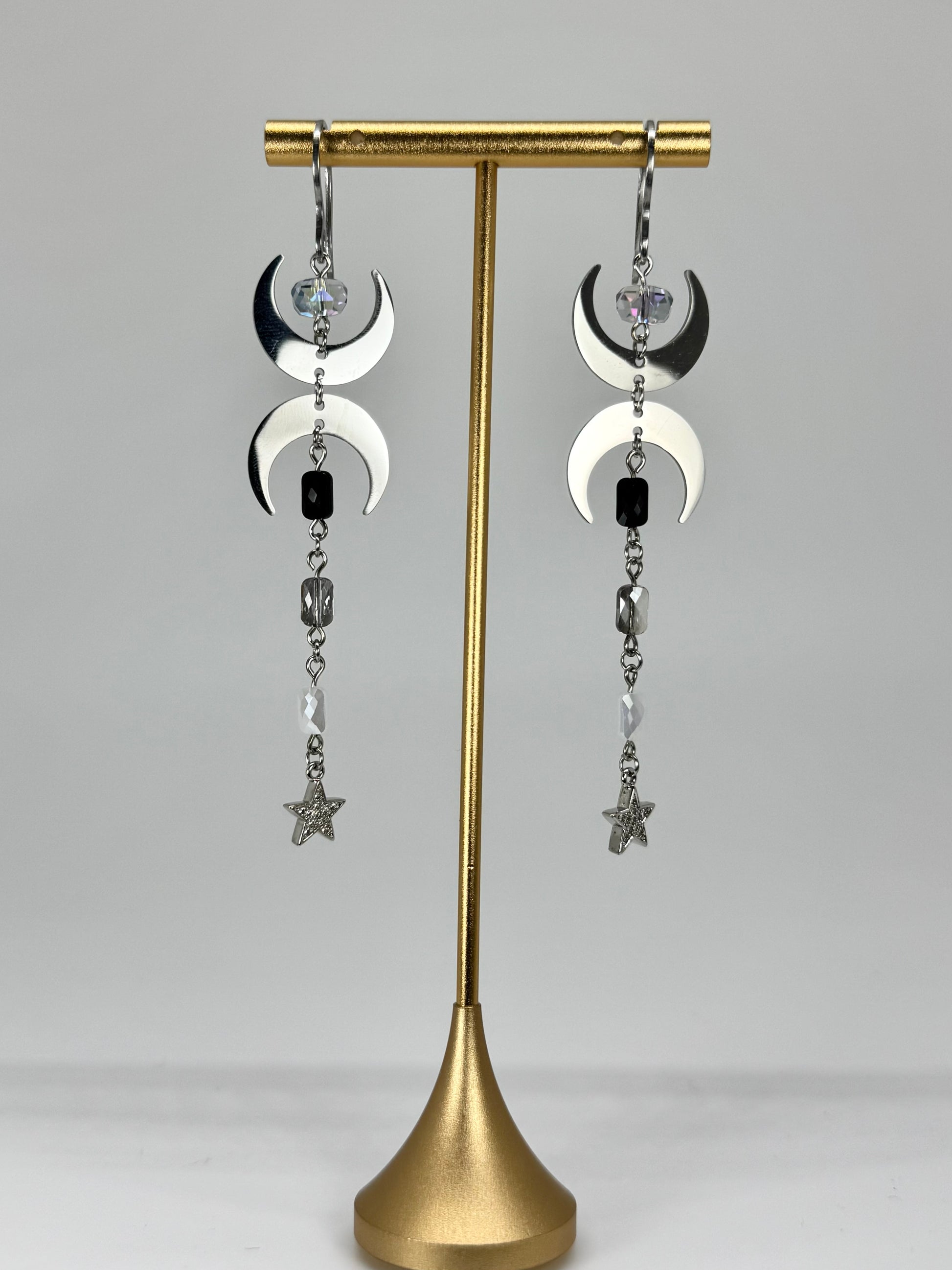 Pair of earrings on a gold stand against a gray background