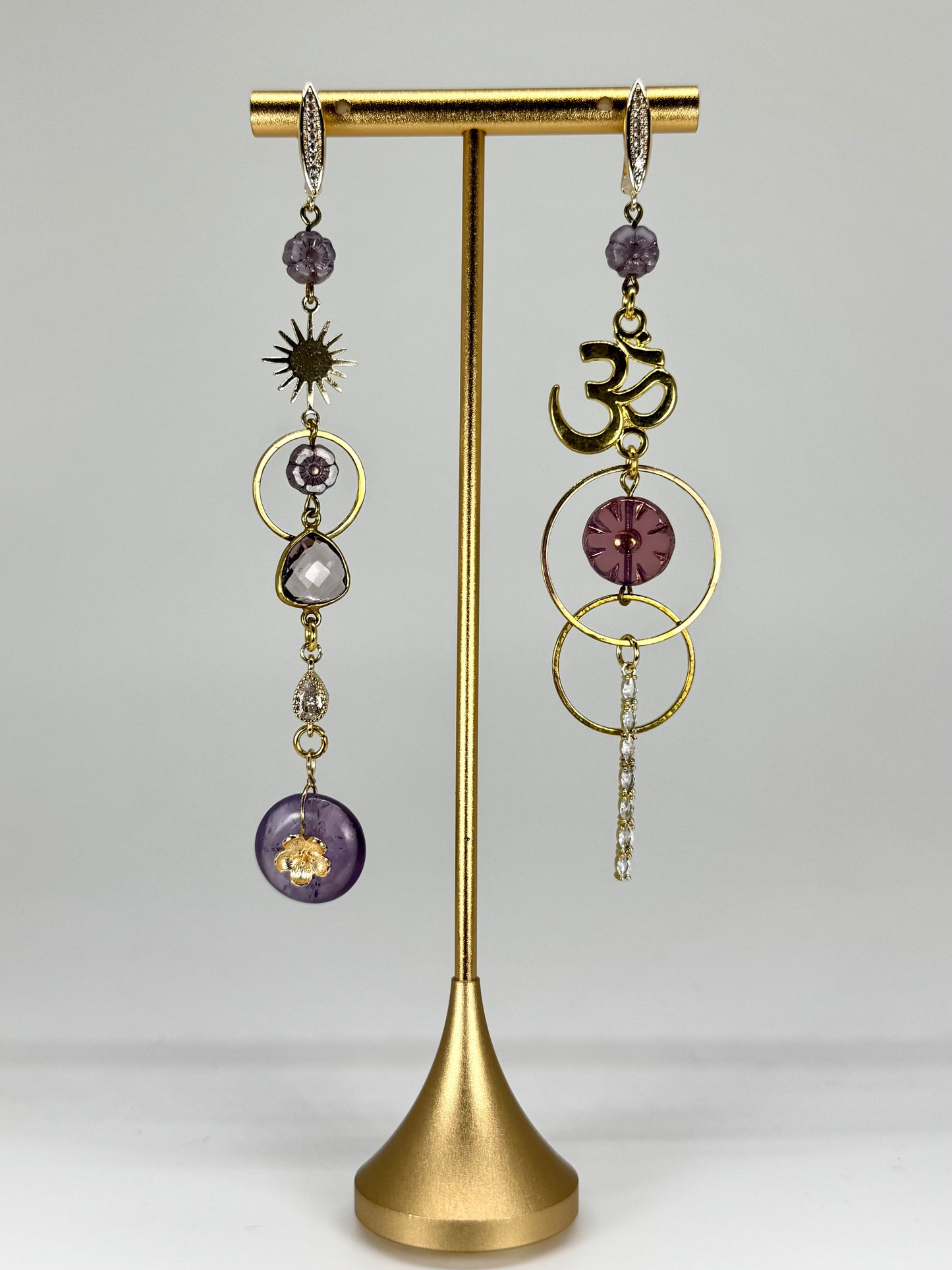 Pair of gold and purple earrings on a gold stand against a gray background